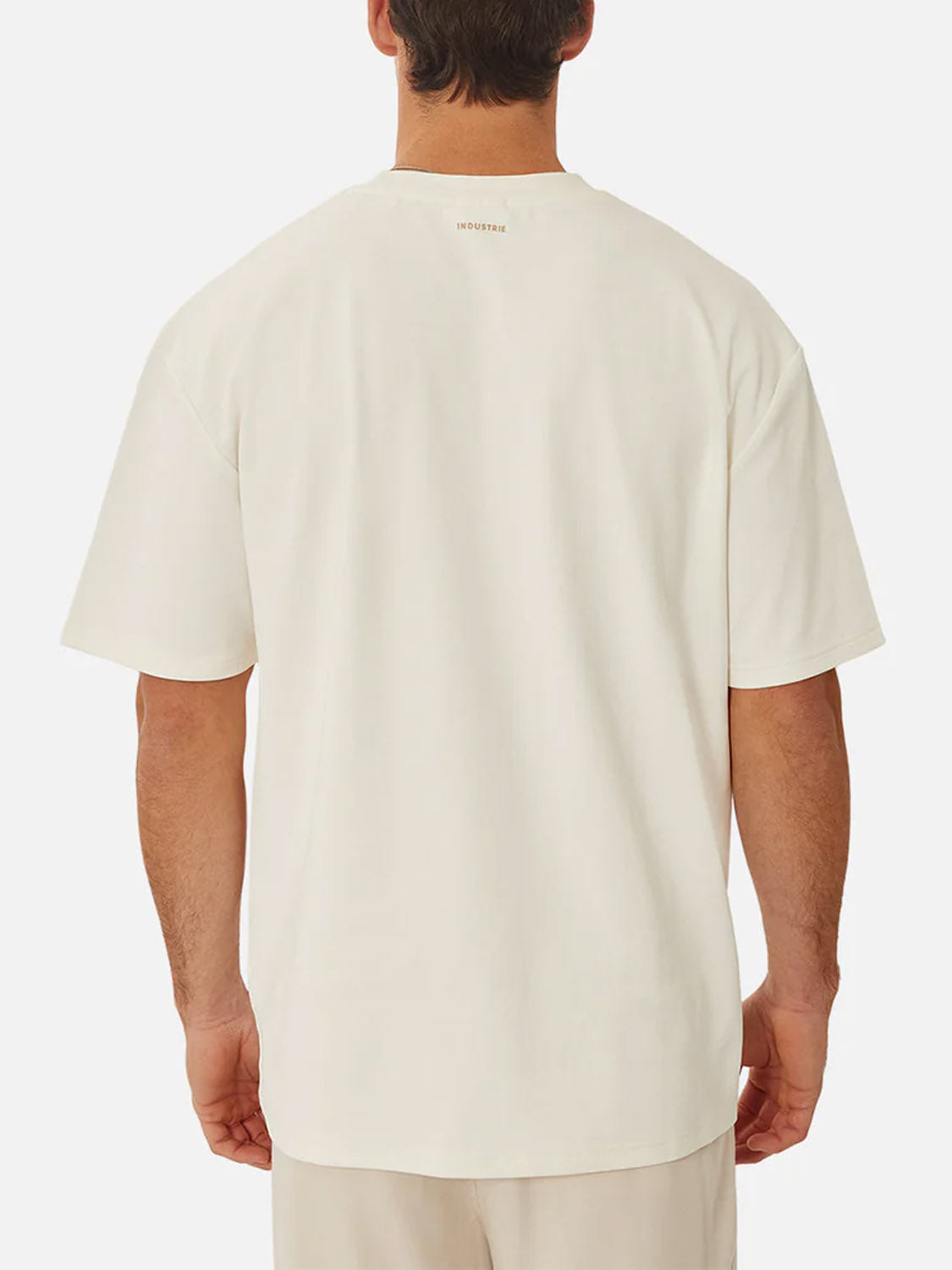 A man is seen from behind wearing Industrie’s The Newport T-Shirt, an oversized heavyweight crew neck with short sleeves, paired with light-colored shorts. The plain white background keeps the focus on the outfit.