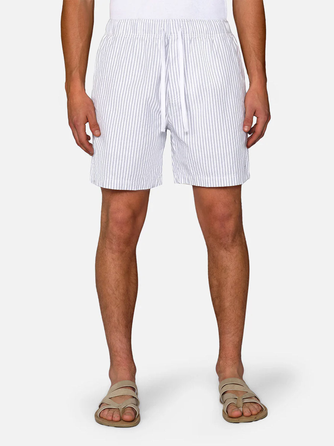 A person wears Industrie’s The New Southwest Short in light blue and white vertical stripes (100% linen), paired with a white top and beige sandals, standing facing forward against a plain background.
