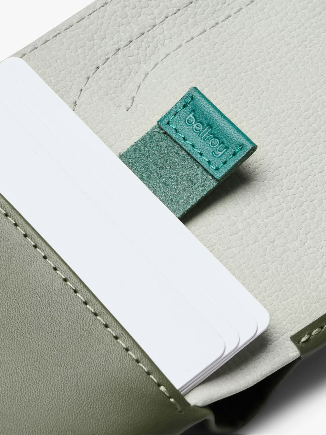 A close-up of the Bellroy Note Sleeve Wallet in green, featuring white cards partially visible and a green fabric pull tab labeled "bellroy" inside the leather billfold.