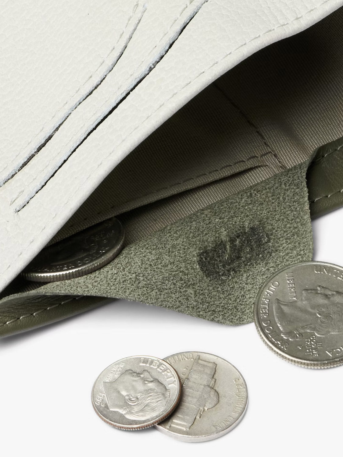 A close-up of the Bellroy Note Sleeve Wallet, a slim leather billfold in light gray, partially open with several US coins inside—including nickels and quarters—and a few more scattered on the surface.