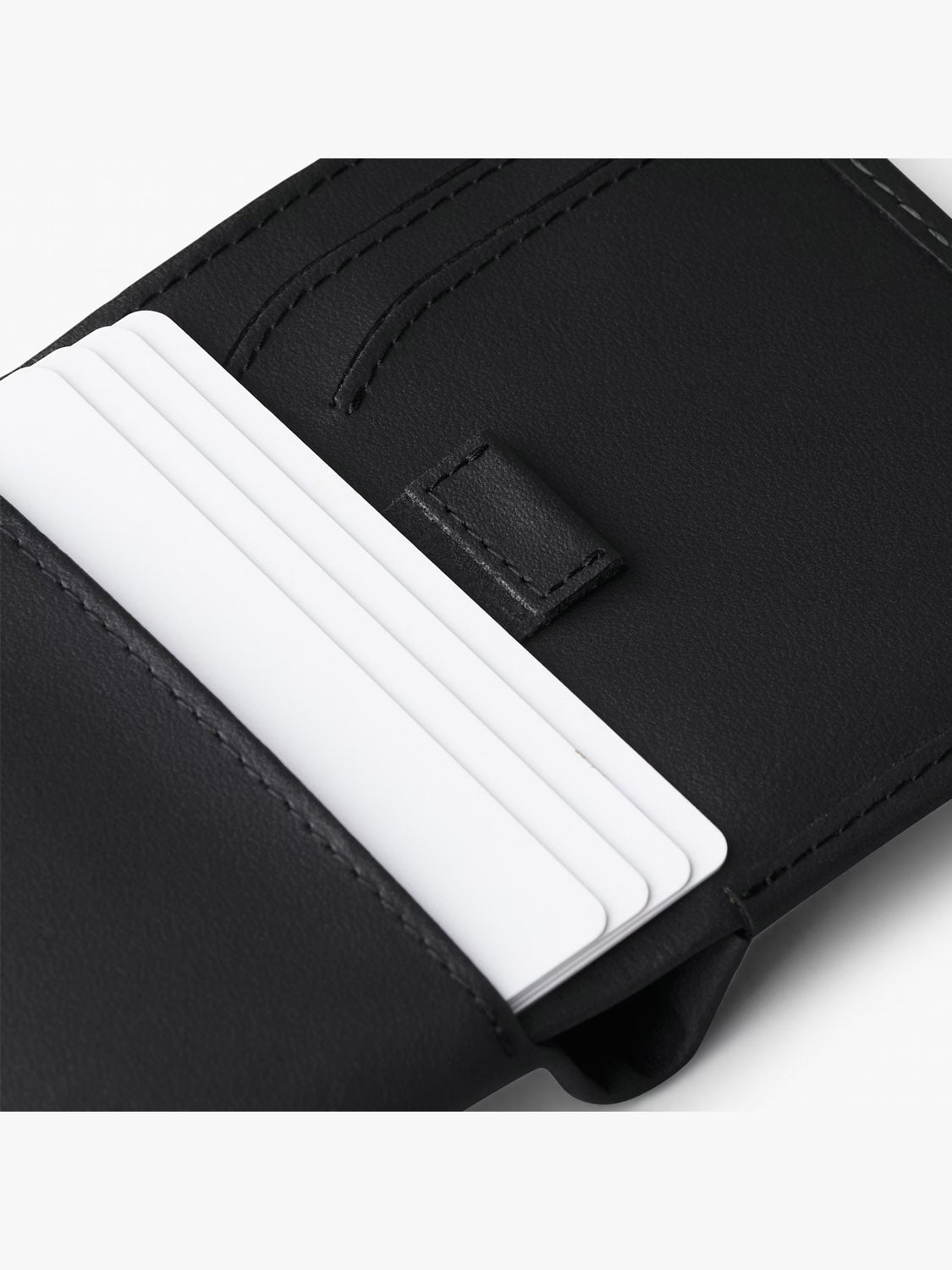 Close-up of the Bellroy Note Sleeve Innovera™ Edition—a sleek black leather billfold with RFID protection. Several white cards in its slots emphasize its precise stitching and thoughtful compartment design.