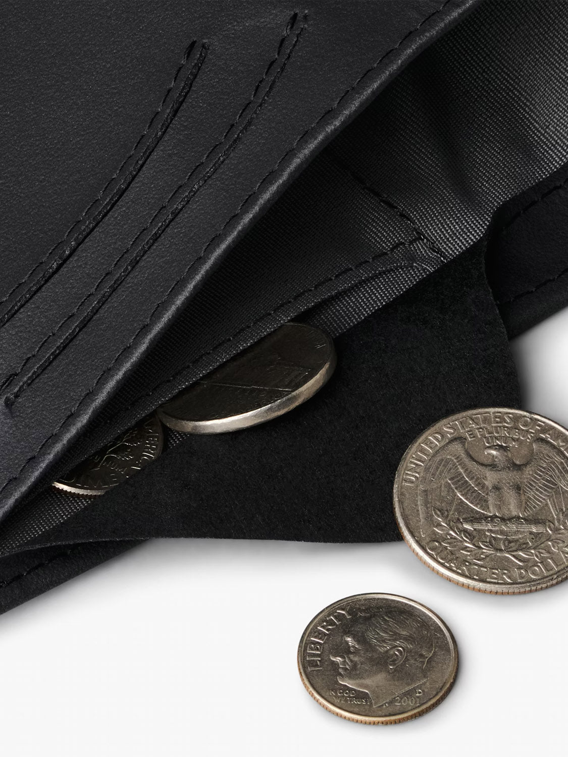 A close-up of an open Bellroy Note Sleeve Innovera™ Edition, a sleek leather alternative wallet with RFID protection, holding several U.S. coins—including a quarter and a dime—scattered on a white surface.