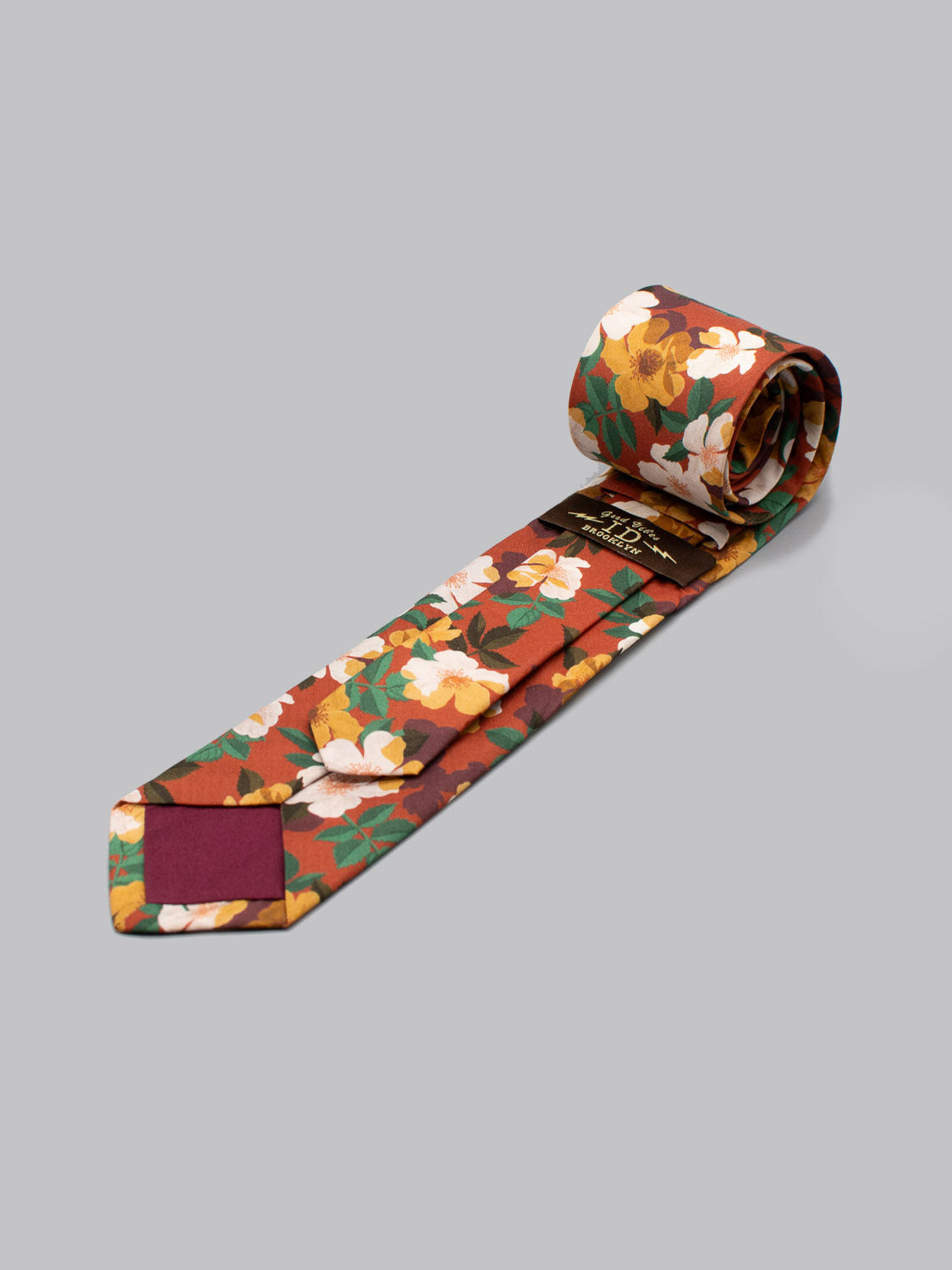 The Liberty of London Tana Lawn™ Nysa Tie by ID Menswear features yellow, white, and green floral patterns on a red background, displayed rolled on a plain gray surface.