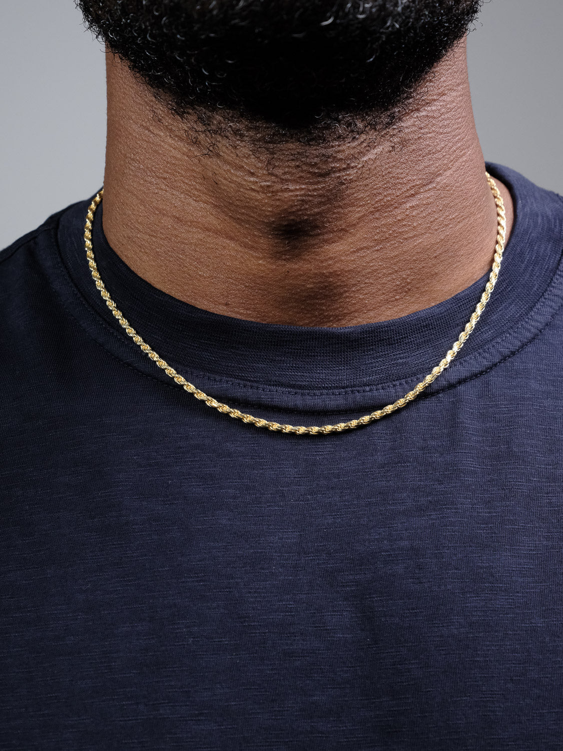 A close-up of a person wearing the Orion 60 Rope Chain Necklace by ID Menswear, featuring a gold-plated 925 Sterling Silver design over a dark navy blue t-shirt. Only the lower face, neck, and upper chest are visible.
