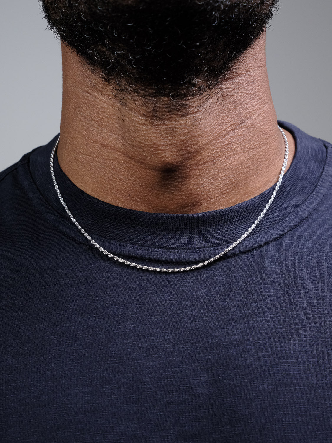 A close-up of a person wearing the Orion 40 Rope Chain Necklace by ID Menswear and a dark blue crew-neck t-shirt. The lower face and neatly trimmed beard are partially visible.