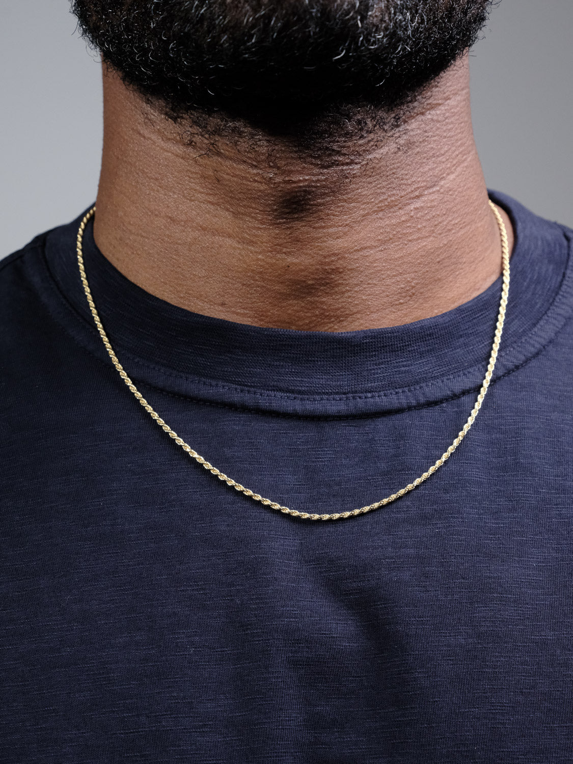 A close-up of a person wearing a navy blue crew-neck shirt and the Orion 40 Rope Chain Necklace by ID Menswear, showing only the lower half of their face, neck, and upper chest.