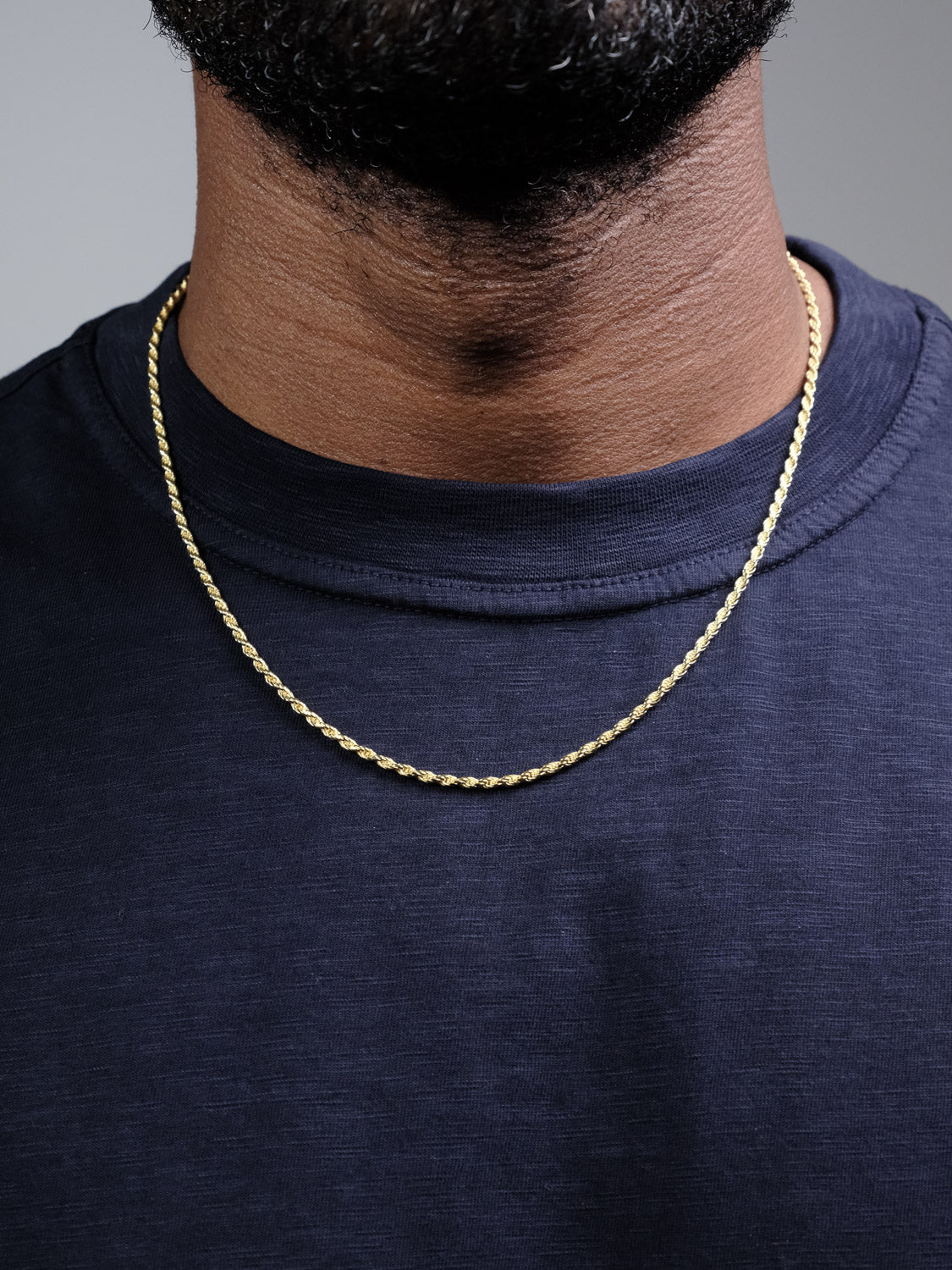 A close-up of a person wearing the Orion 50 Rope Chain Necklace by ID Menswear over a dark navy blue t-shirt, showing only the lower part of their face and neck.