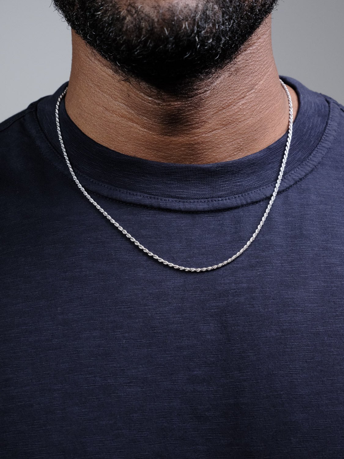 A close-up shows the lower face and neck of a person wearing the Orion 40 Rope Chain Necklace by ID Menswear with a dark navy crew-neck shirt.