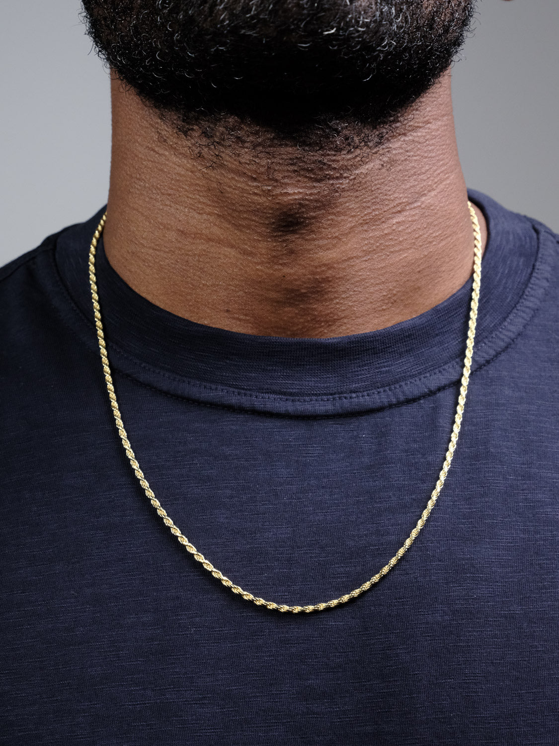 A close-up of a person wearing the Orion 50 Rope Chain Necklace by ID Menswear—4mm, made in Italy—over a dark blue crew-neck shirt, showing just the neck, lower face, and upper chest.