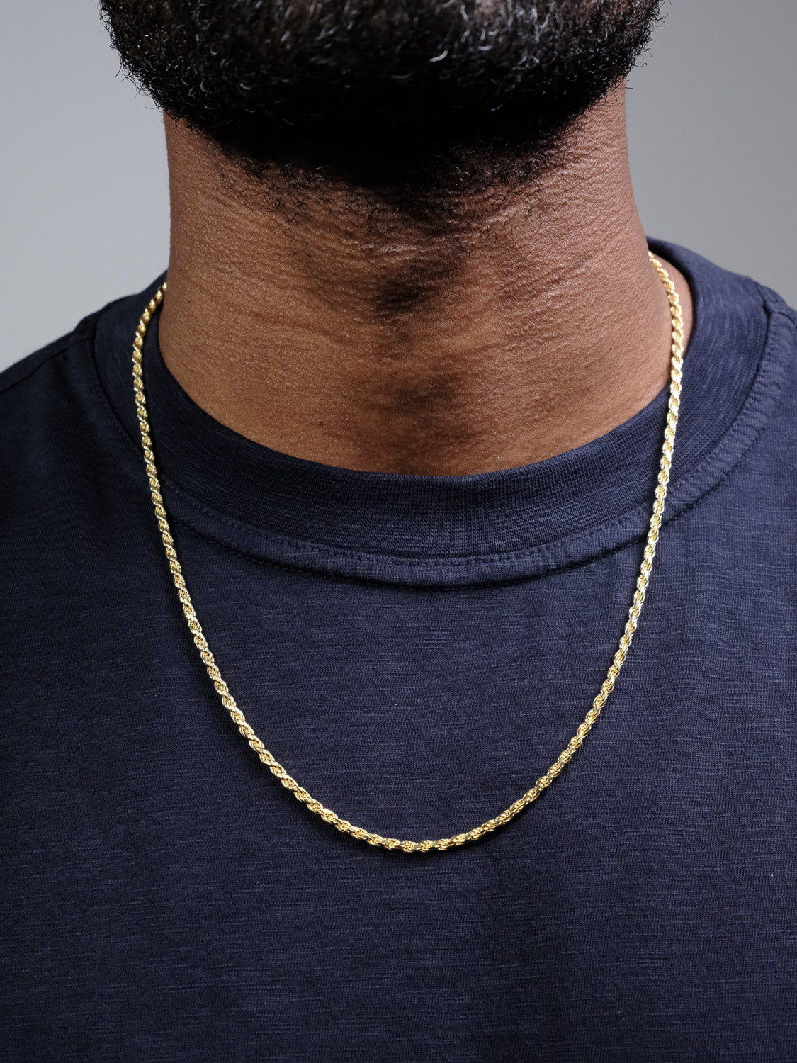 A close-up of a person wearing the Orion 60 Rope Chain Necklace by ID Menswear over a dark navy blue shirt, with the lower part of their bearded face visible.