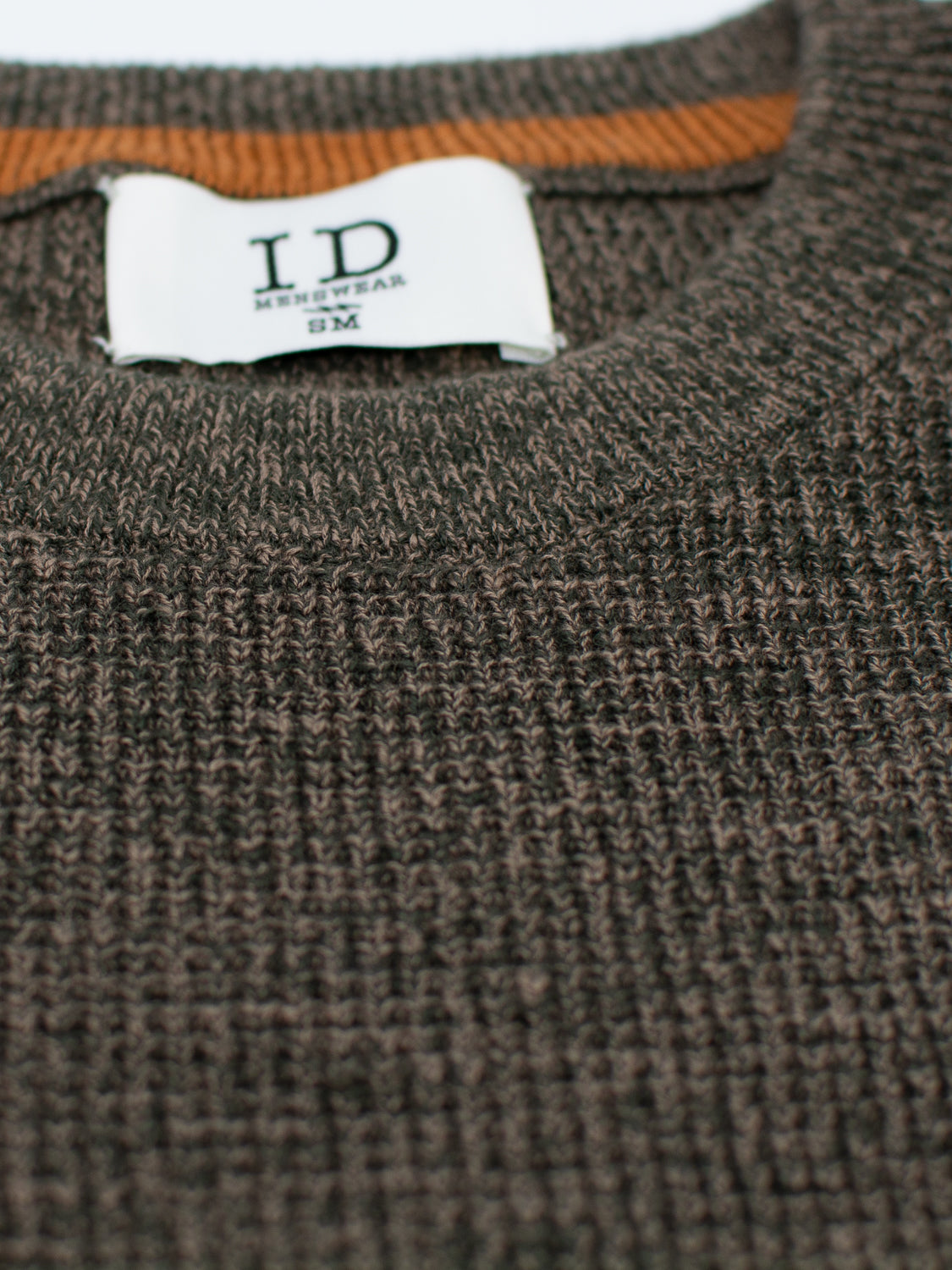 Close-up of the Oslo Waffle Knit Sweater by ID Menswear, featuring a brown knitted fabric with a ribbed texture similar to waffle knit sweaters. The orange accent on the neckline enhances its casual wear charm, and a visible clothing label adorns the collar.