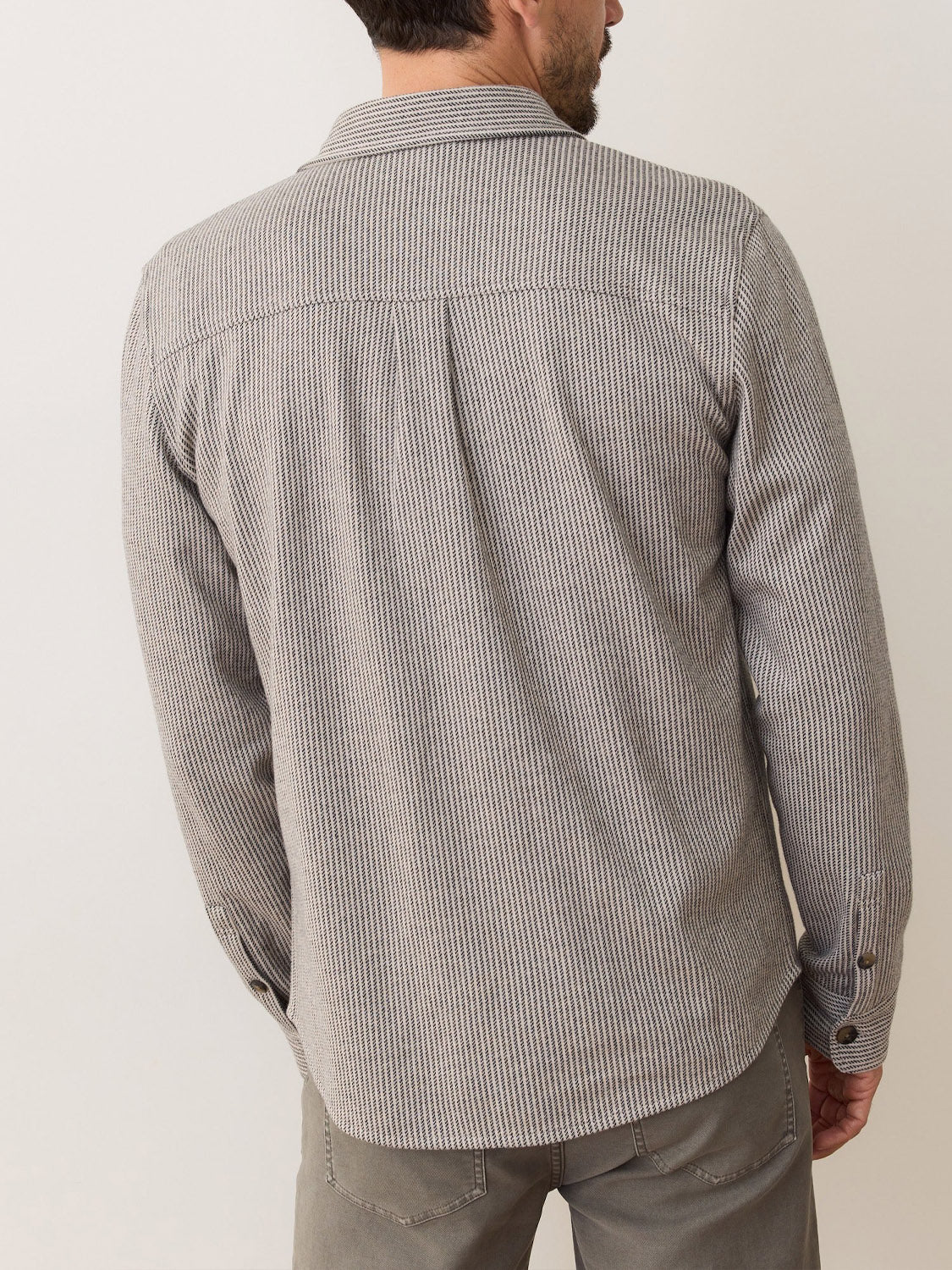 A man is seen from behind wearing a Marine Layer Pacific Stretch Grey Twill Overshirt with light gray pants, set against a plain off-white background.