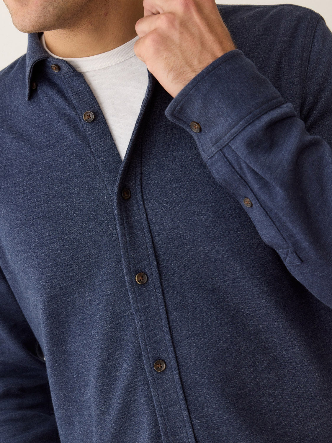 A person wears a Marine Layer Pacific Stretch Twill Shirt in navy over a white tee, touching the collar. The cropped image focuses on the upper torso and face, highlighting the men's overshirt and its soft stretch twill fabric.