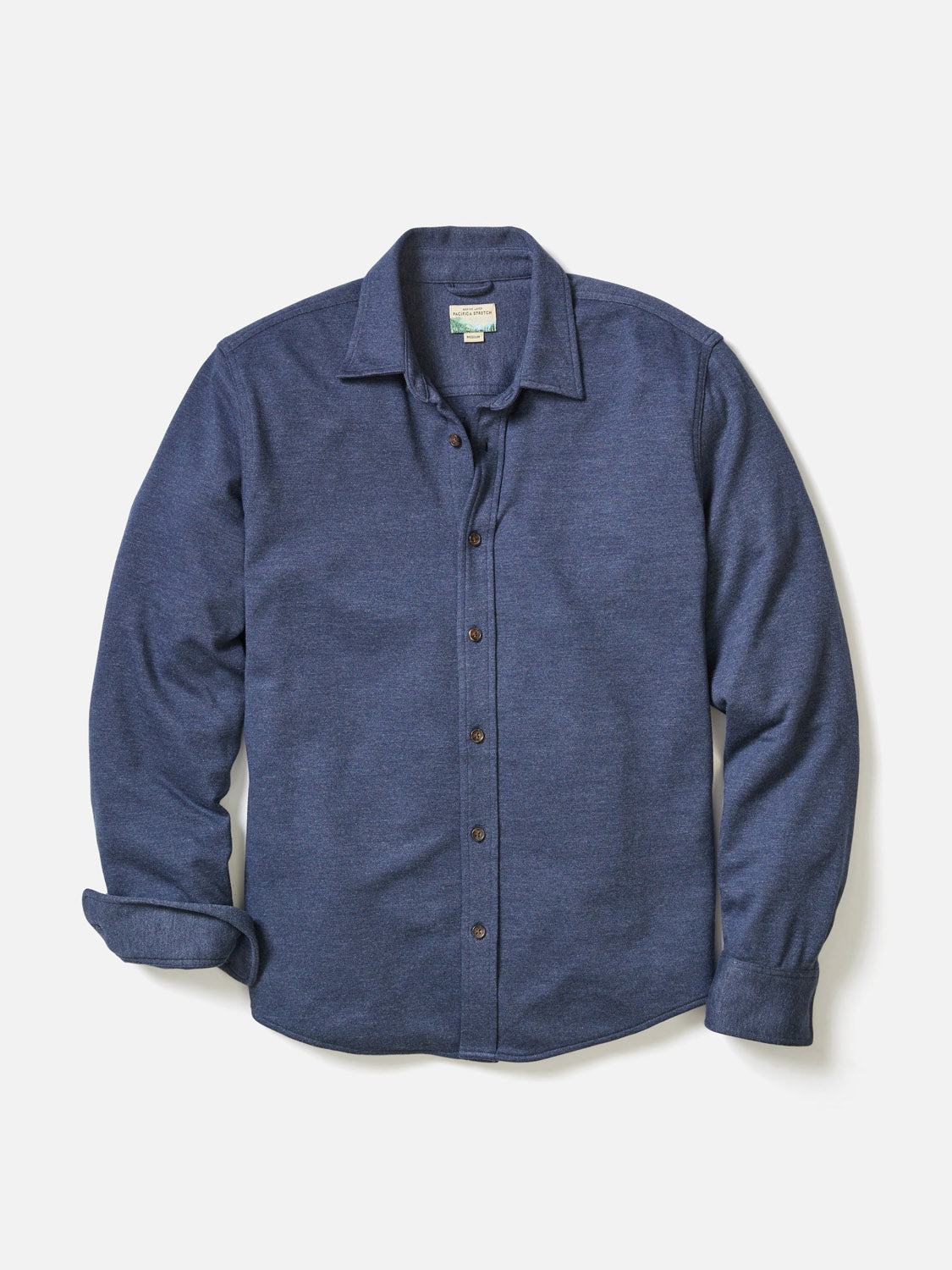 The Marine Layer Pacific Stretch Twill Shirt is a men's long-sleeve button-up overshirt in solid dark blue, crafted from soft stretch twill, with brown buttons, a classic collar, and one sleeve slightly rolled up, shown flat on white.