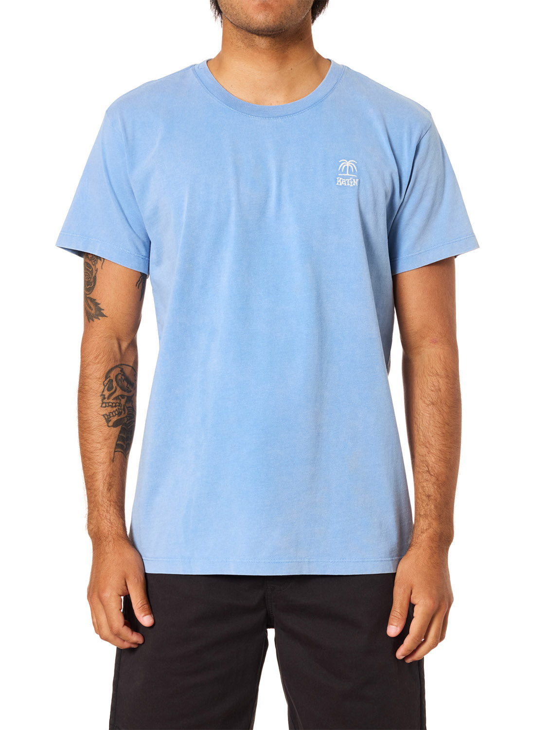 A person in a light blue Katin K-Palm Embroidered Tee with a white palm tree graphic on the chest and black shorts stands against a plain white background, their face partially out of frame.