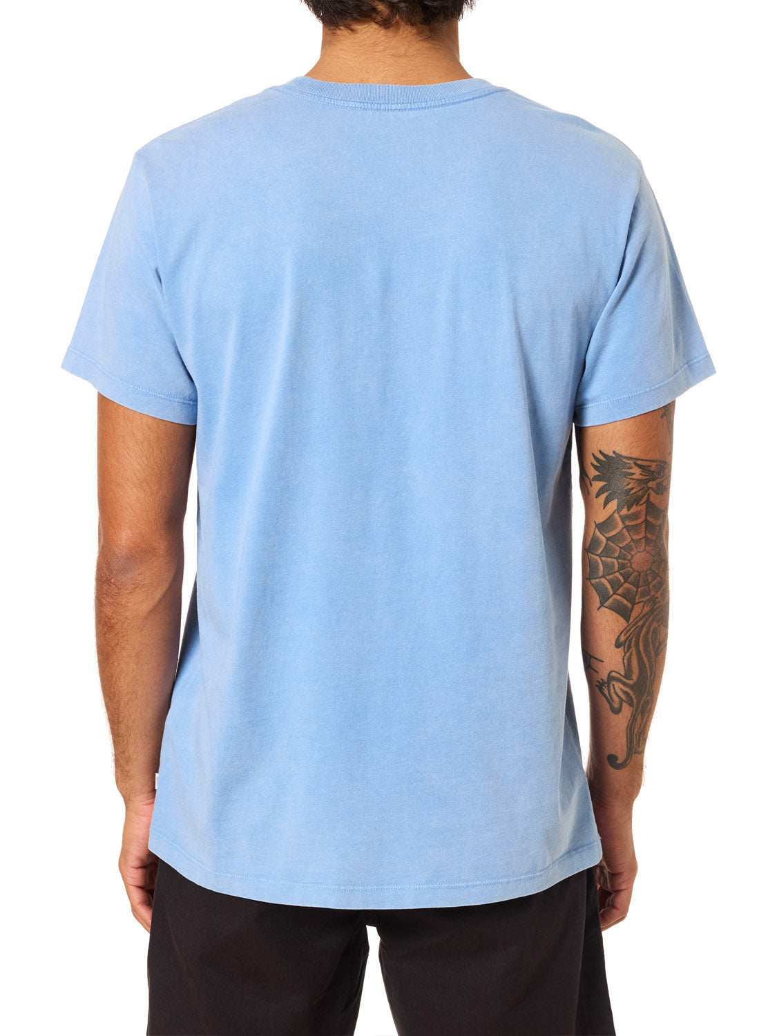 A person with short dark hair, seen from behind, wears the Katin K-Palm Embroidered Tee by Katin in light blue organic cotton and black shorts. A large dragon tattoo is visible on their right arm.