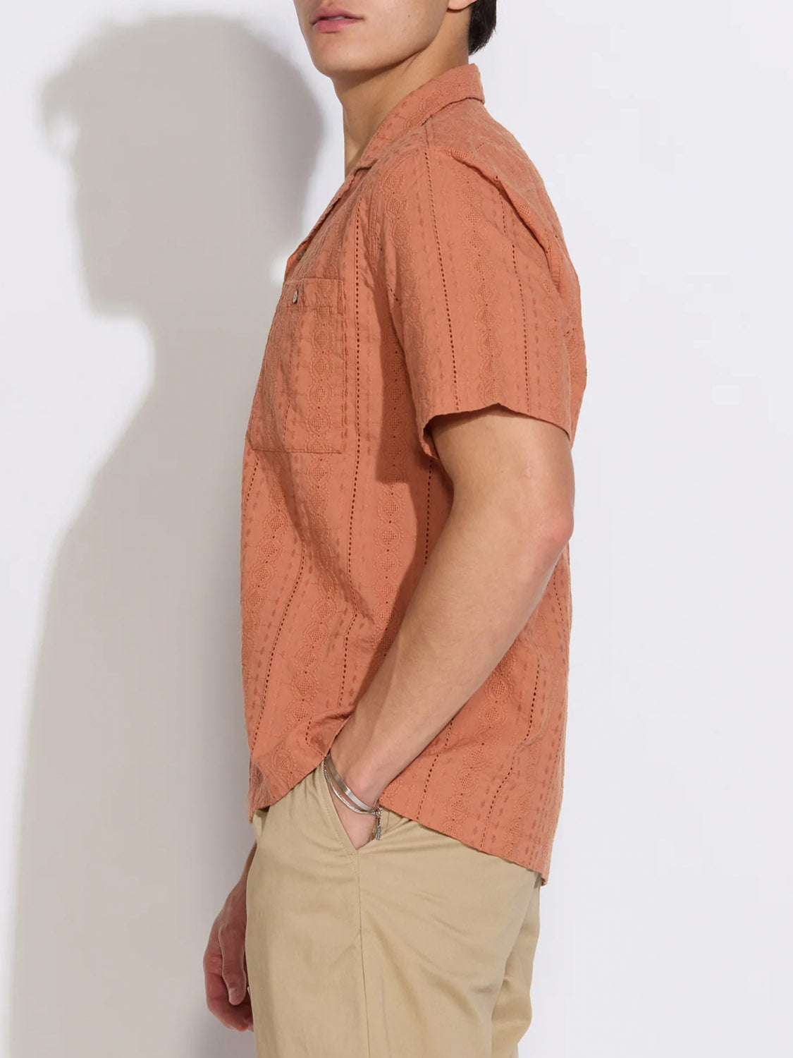 A person stands in profile against a white background, wearing the Civil Society Palomino Relaxed Fit Pocket Resort Shirt in light orange and beige pants. One hand is in their pocket, with their face partially out of frame.