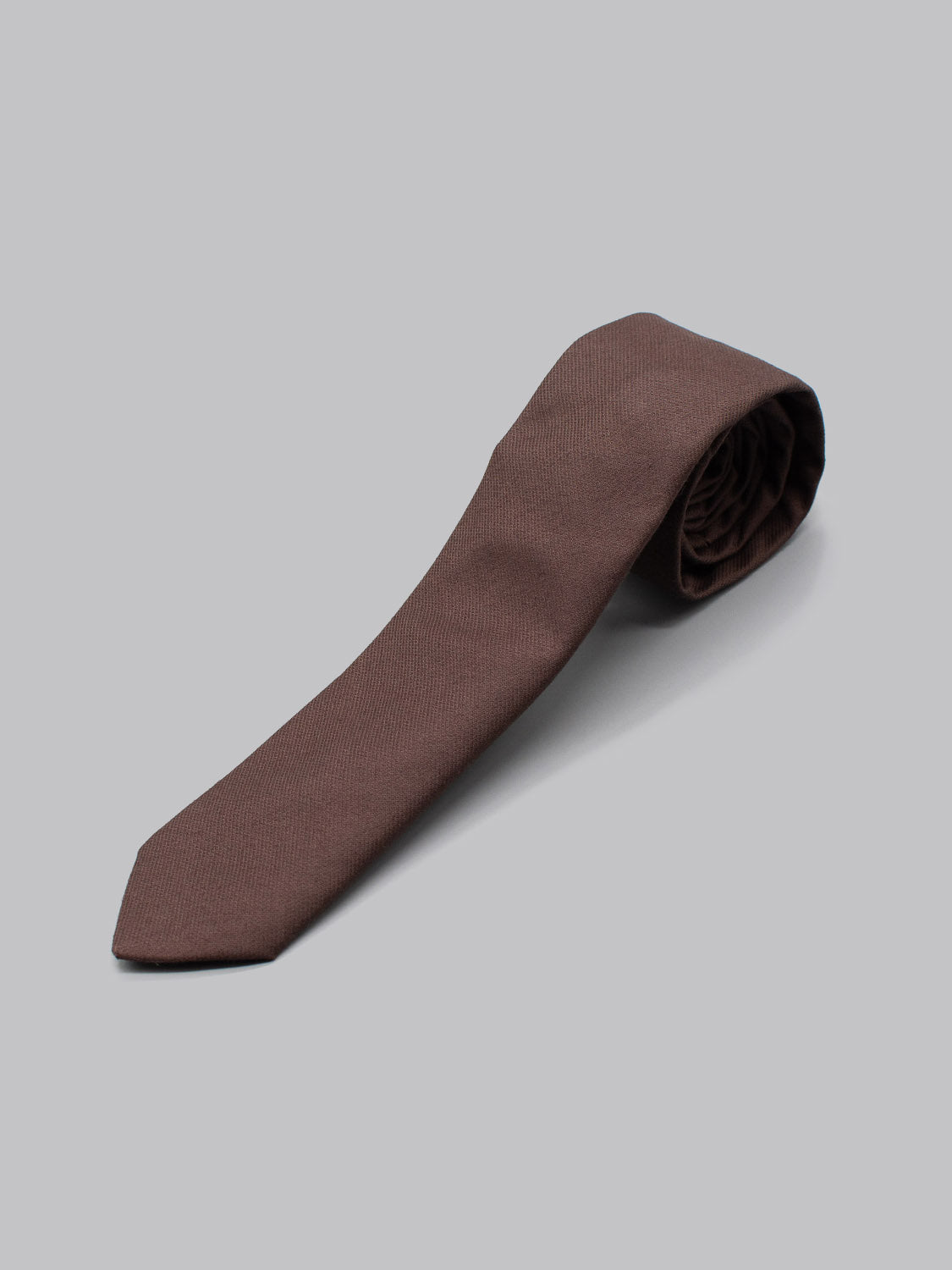 The ID Cotton Tie Paris by ID Menswear, handmade from brown cotton in Brooklyn, is neatly rolled at one end and displayed on a plain light gray background.