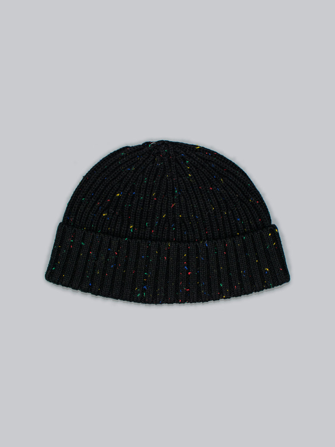 The ID Menswear Paro Speckled Cotton Fishermans Beanie, crafted with speckled yarn, lies on a light gray background, showcasing its dark ribbed knit design and timeless multicolored speckles for added flair.