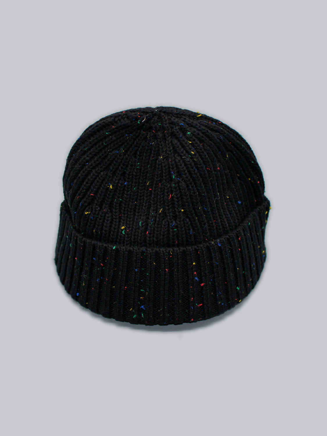 The Paro Speckled Cotton Fishermans Beanie from ID Menswear is a black knit beanie with a timeless design, speckled yarn, folded brim, and ribbed texture, shown on a plain light grey background.