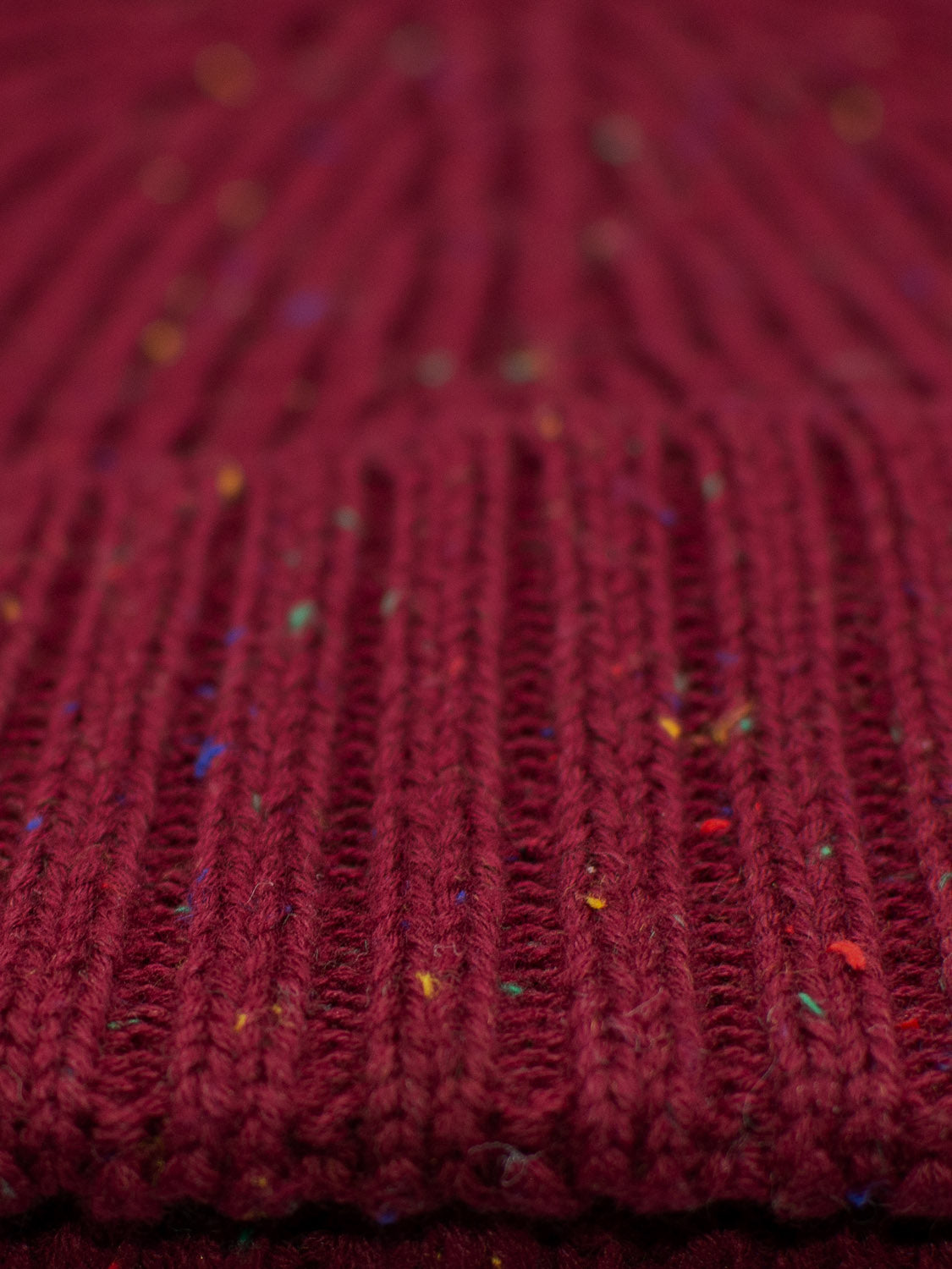 A close-up of maroon ribbed knit fabric, with subtle multicolored speckles, crafted from speckled yarn, reminiscent of the timeless ID Menswears Paro Speckled Cotton Fishermans Beanie.