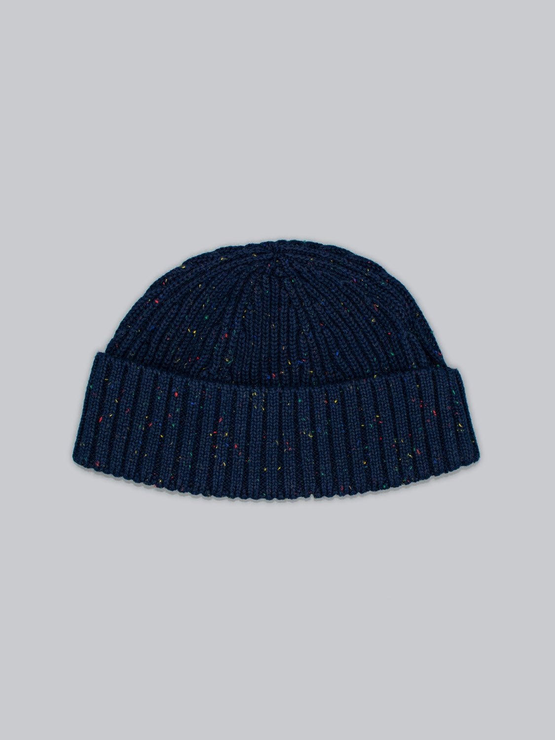 The Paro Speckled Cotton Fishermans Beanie from ID Menswear is a knitted dark blue, ribbed accessory made of cotton with speckled yarn. It stands out against a plain gray background, highlighting its colorful design.