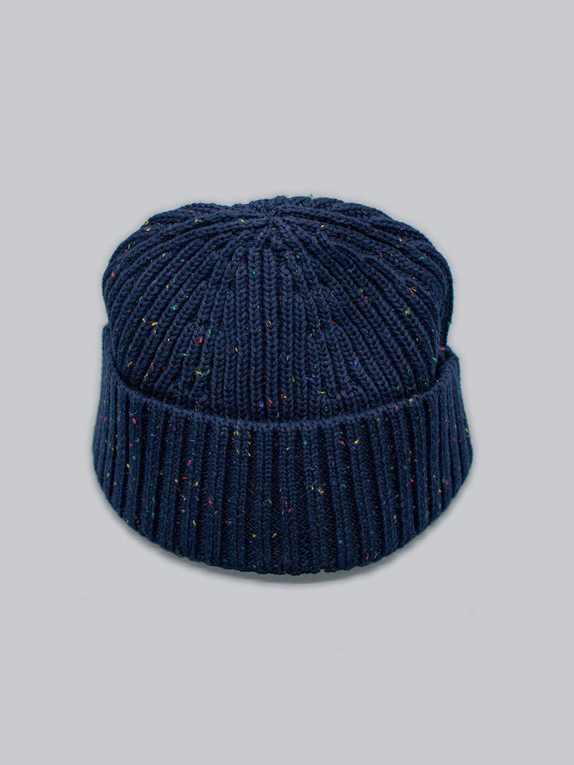 Introducing the Paro Speckled Cotton Fishermans Beanie by ID Menswear, featuring navy blue with colorful speckled yarn on a gray background. This timeless design has a folded cuff and ribbed pattern, perfect for any style.