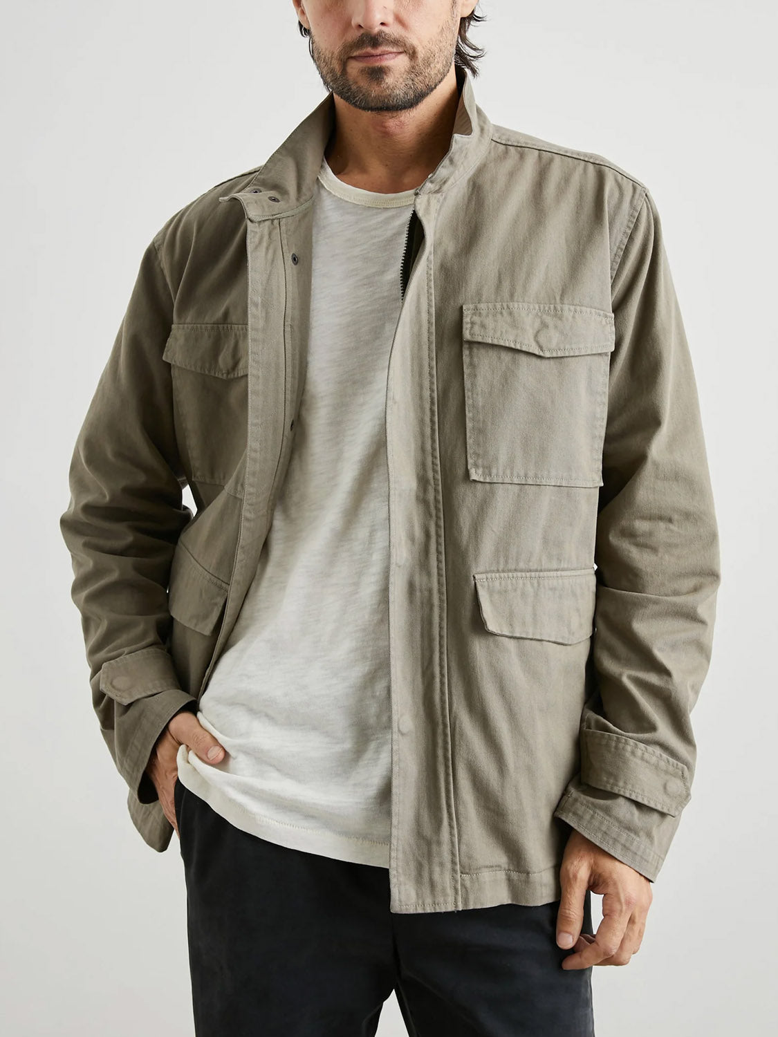 A man models the Rails Paulsen Jacket in light khaki over a white tee and dark pants, standing with one hand in his pocket against a plain background.