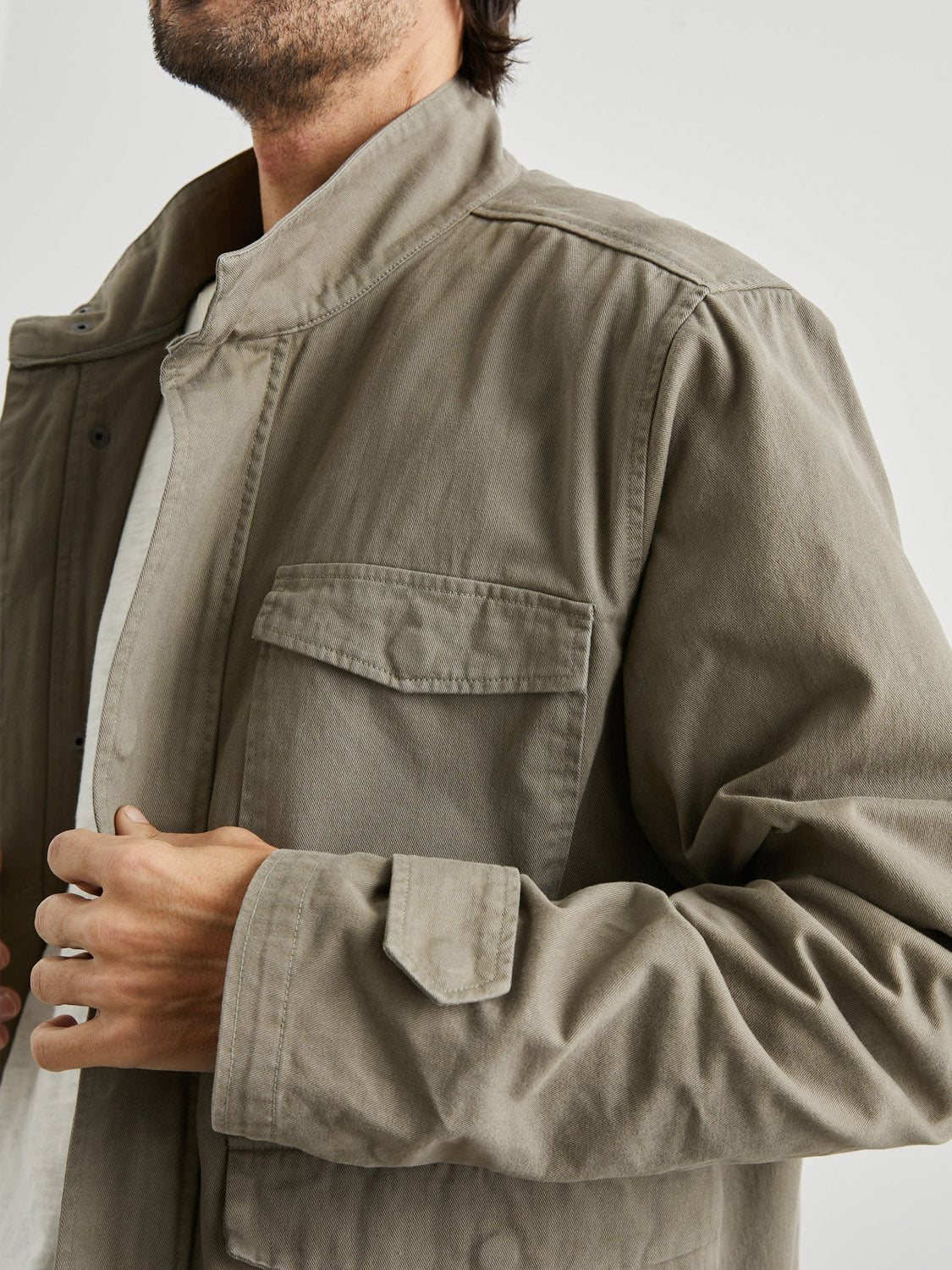 A man wearing the Rails Paulsen Jacket in light brown cotton over a white shirt, shown from shoulders to mid-torso, with one hand adjusting the front of the lightweight jacket.