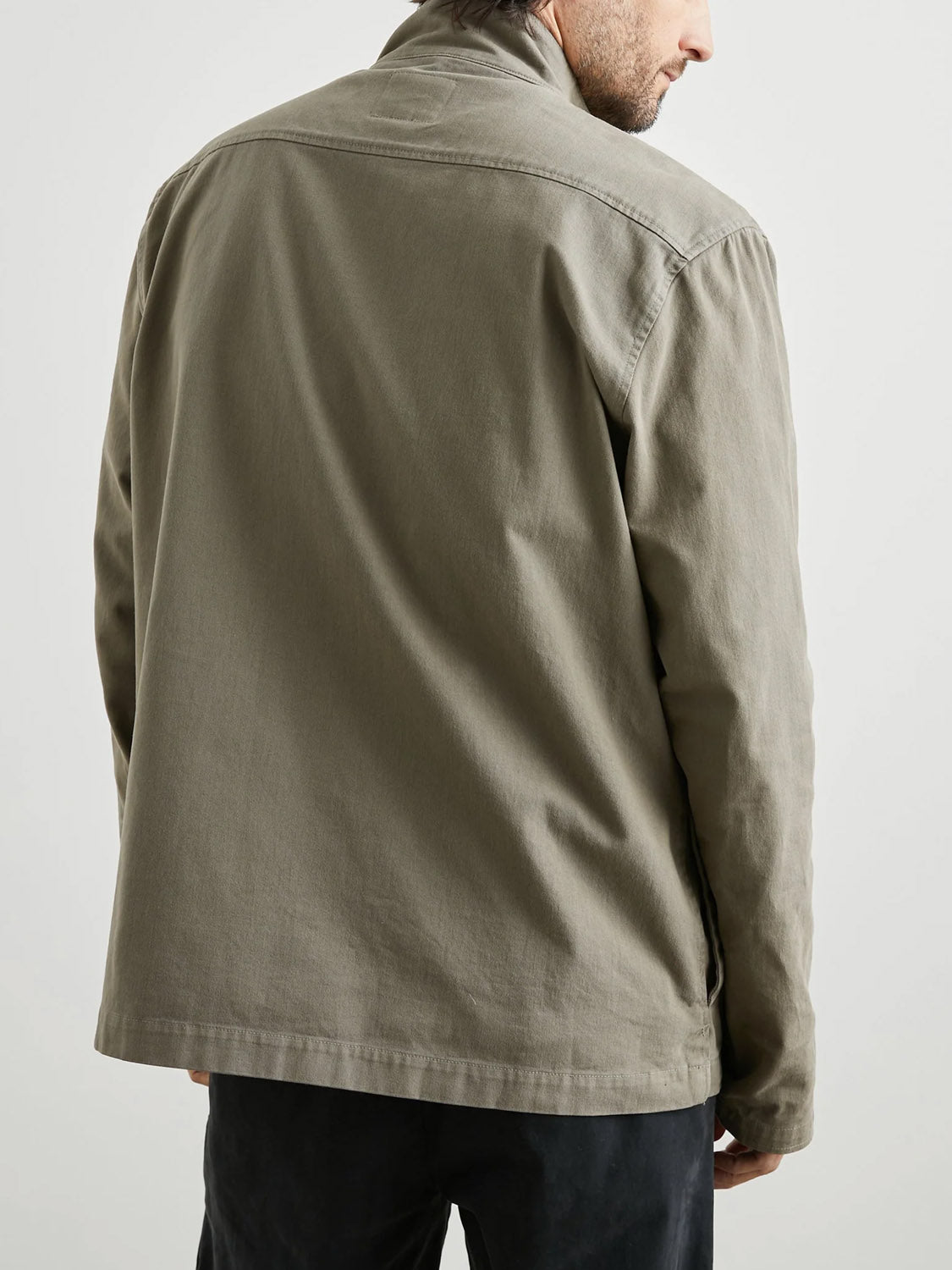 A man is shown from the back wearing the Rails Paulsen Jacket in light olive green with dark pants, standing against a plain light background.