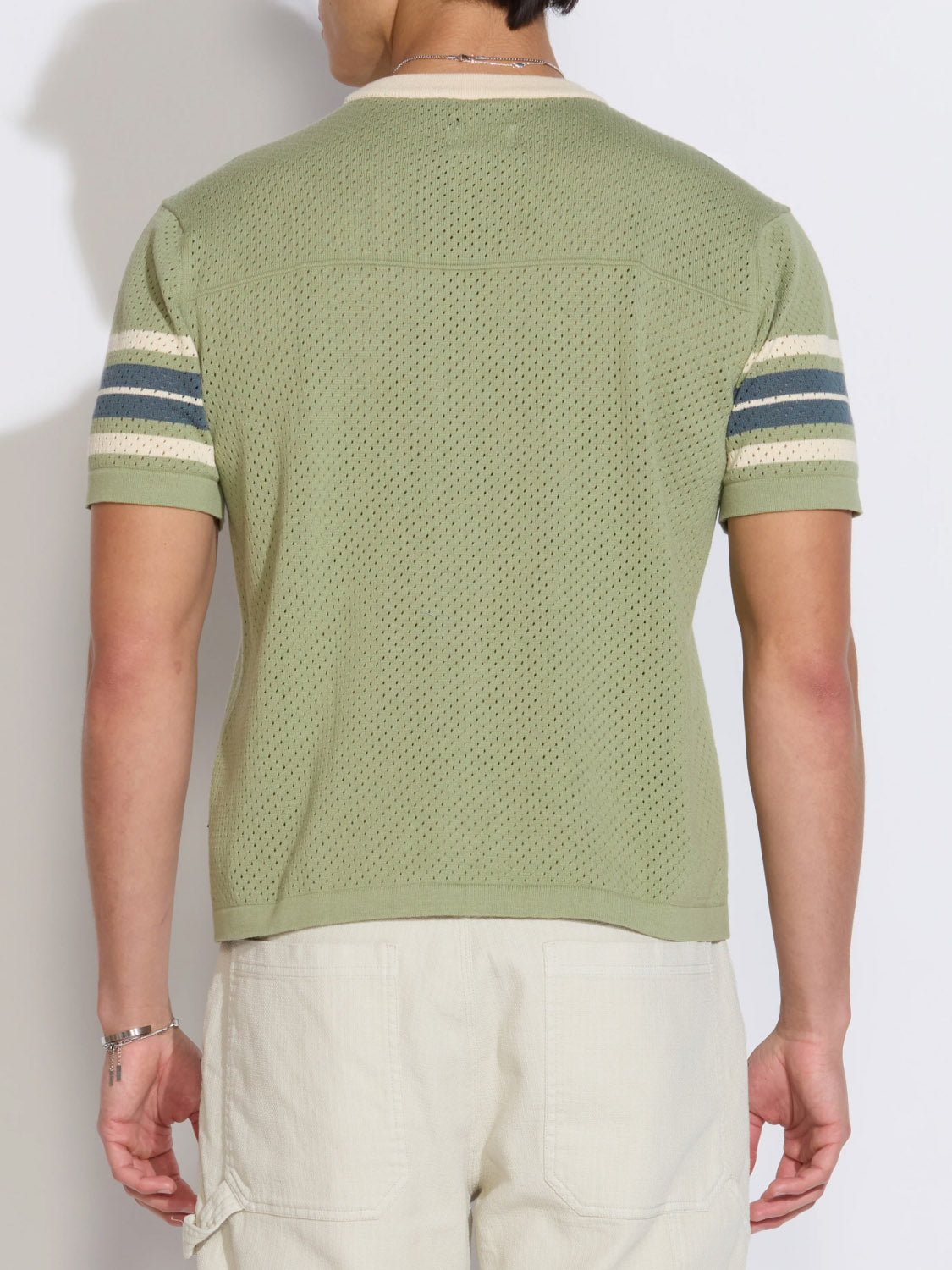 A person is seen from the back wearing the Civil Society Pensacola Relaxed Fit Sweater Knit Tee in light green with mesh-style knit, striped sleeve bands, and light beige pants, set against a plain background.