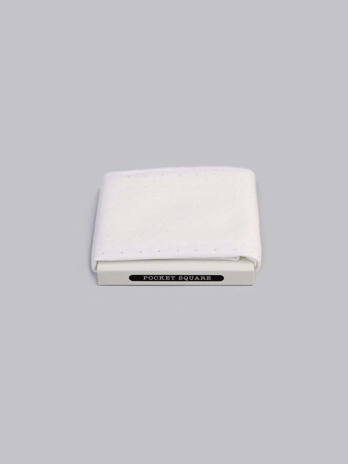 The Perforated White Pocket Square by ID Menswear, crafted from 100% cotton with a subtle dotted texture, is hand-made in Brooklyn and displayed on a white box labeled POCKET SQUARE against a simple grey background.