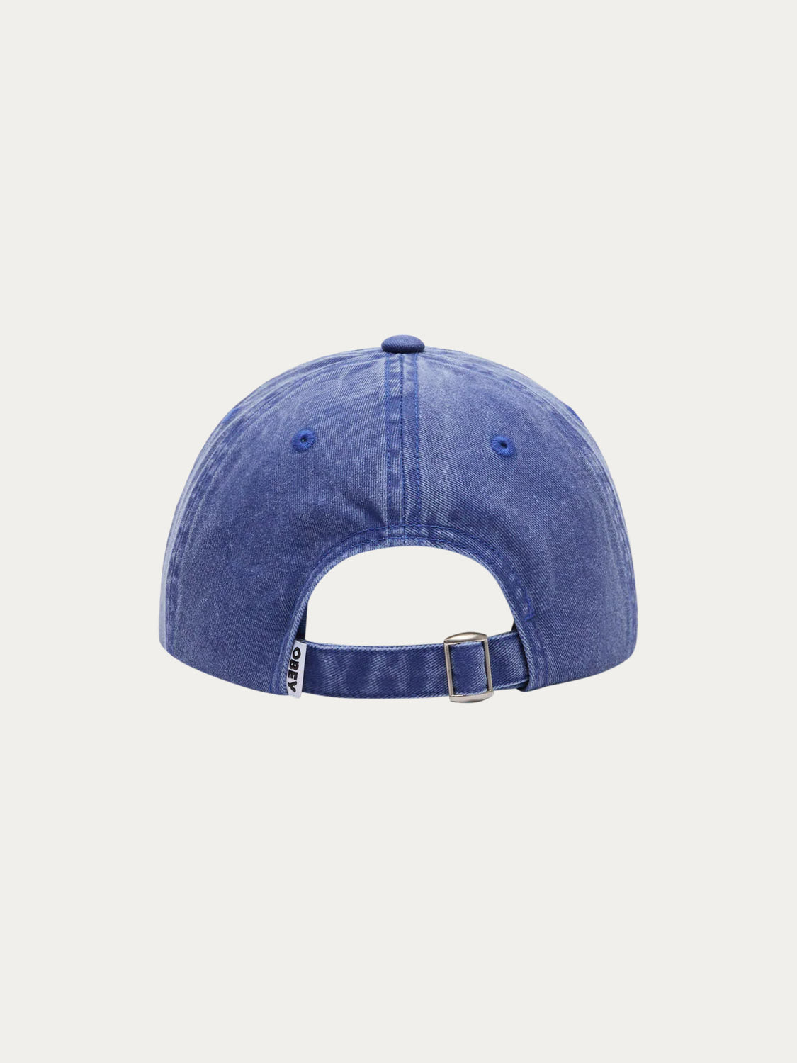 The Obey Pigment Productions SNPB cap is blue denim with a vintage look, a strap-back closure with metal buckle, and a small tag on the left side, shown from the back.