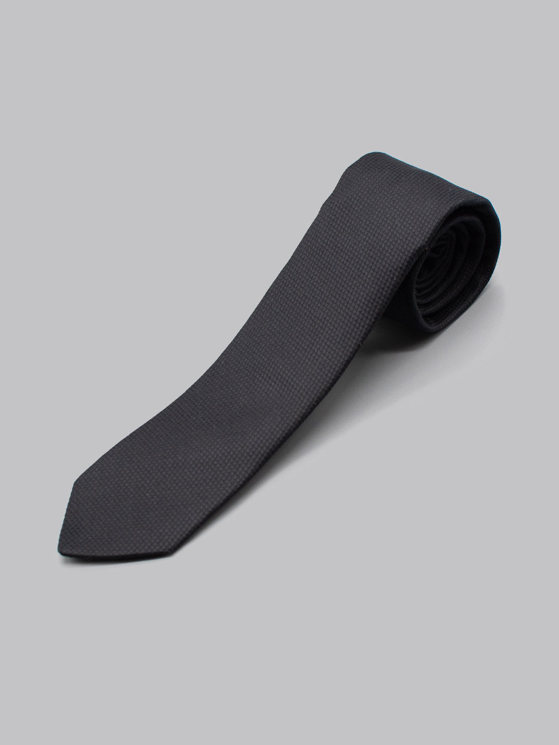 The ID Menswear ID Cotton Tie Pique, a handcrafted dark navy textured cotton tie, is shown neatly rolled on a light grey background.