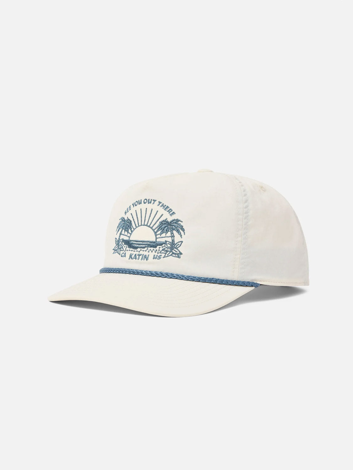 The Katin Playa Hat is a cream 5-panel hat with a blue rope above the brim and a blue sunrise, palm trees, and waves graphic. “SEE YOU OUT THERE KATIN.” appears above the graphic. Features an adjustable snapback closure.