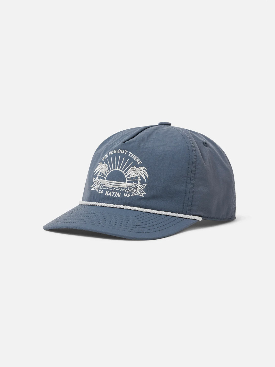The Katin Playa Hat is a blue 5-panel snapback made from recycled nylon, featuring a white sunset, palm trees, and waves embroidery, "SEE YOU OUT THERE" and "KATIN USA" text, plus a white rope detail above the brim.