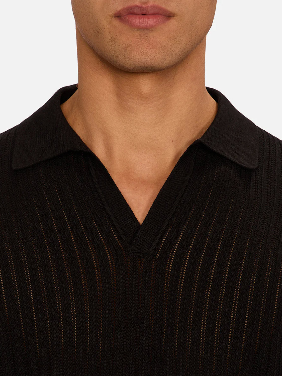 A close-up shows a person wearing the Industrie Poolside Polo, a black knit shirt featuring vertical subtle sheer stripes and a distinctive texture; only the neck, jaw, and upper chest are visible against a plain background.