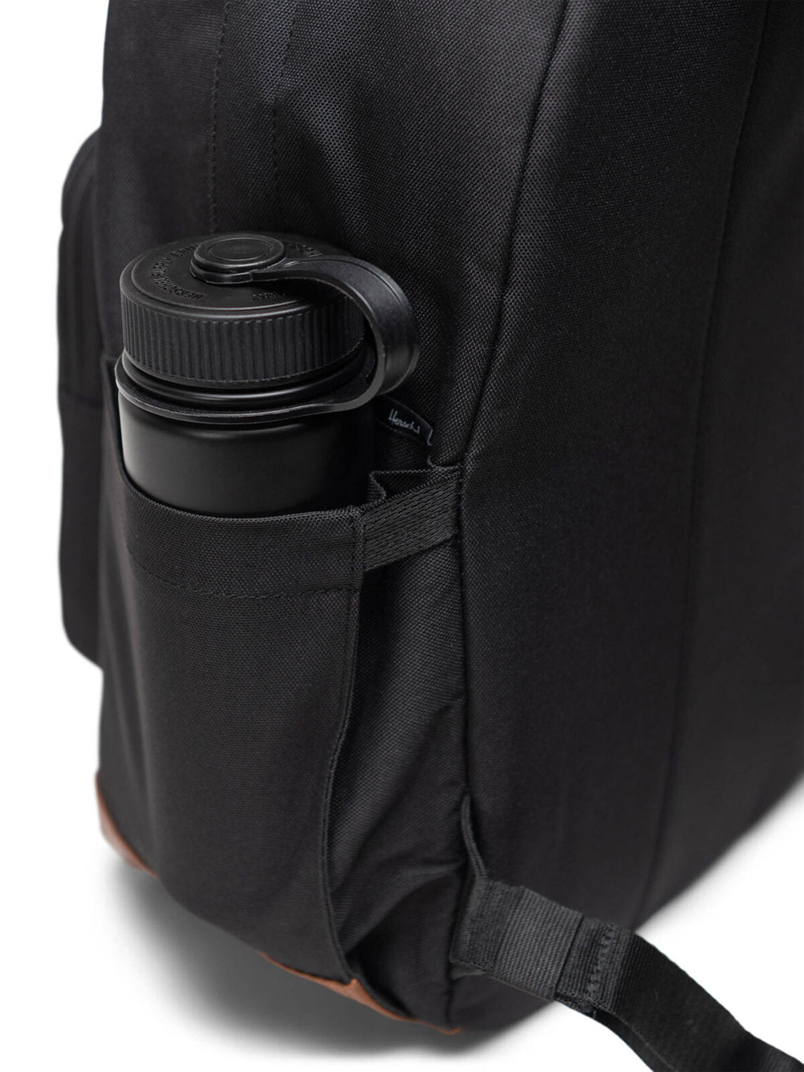 A close-up of the Herschel Pop Quiz Backpack’s side pocket holding a black screw-top water bottle. The recycled black laptop backpack shows its fabric handle, visible stitching, and a small label near the pocket.