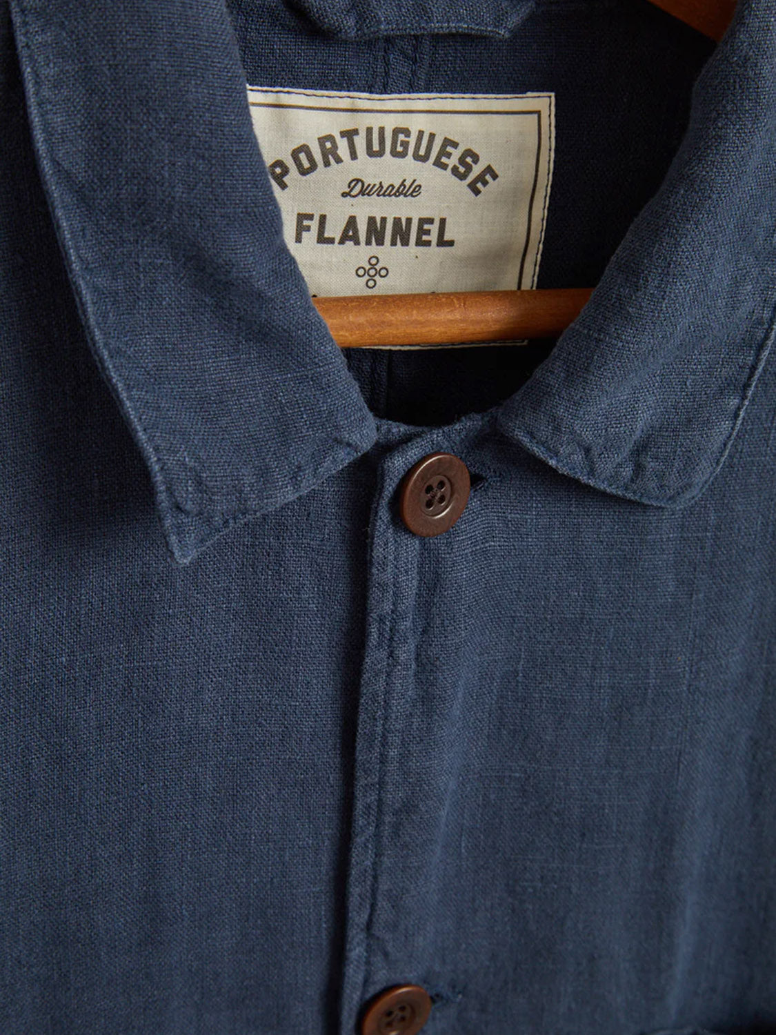 Close-up of a dark blue flannel shirt with brown buttons and an inside collar label reading Portuguese Flannel Labura Linen Jacket, highlighting its link to Portuguese heritage and craftsmanship by quality mills.