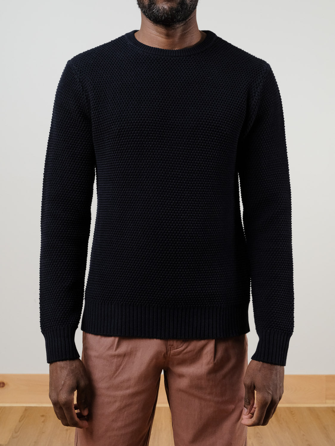 A person wears the Quebec Chunky Knit Sweater by ID Menswear in textured black, paired with light brown pants, standing against a plain white background with arms relaxed at their sides.