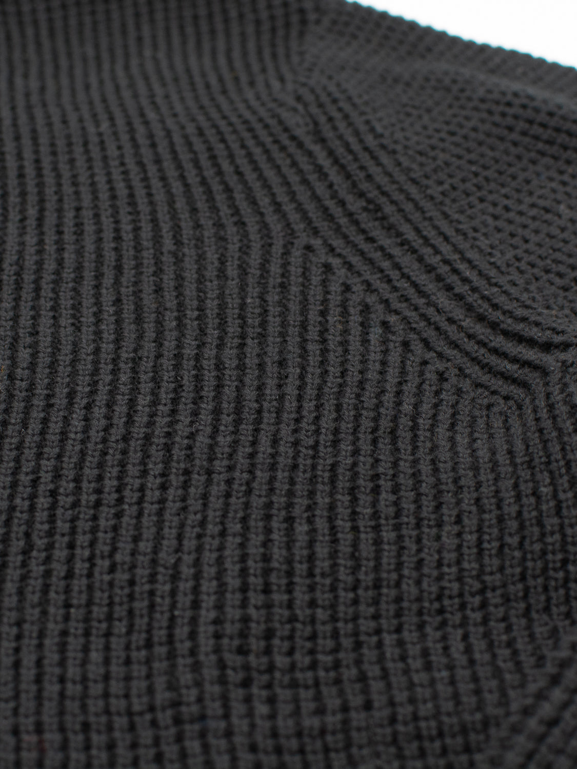 Close-up of ID Menswears Ragnar Waffle Knit Sweater, showcasing its black 100% cotton fabric with a ribbed texture. The tightly packed vertical lines create a structured yet soft look, with lighting highlighting its intricate weave.