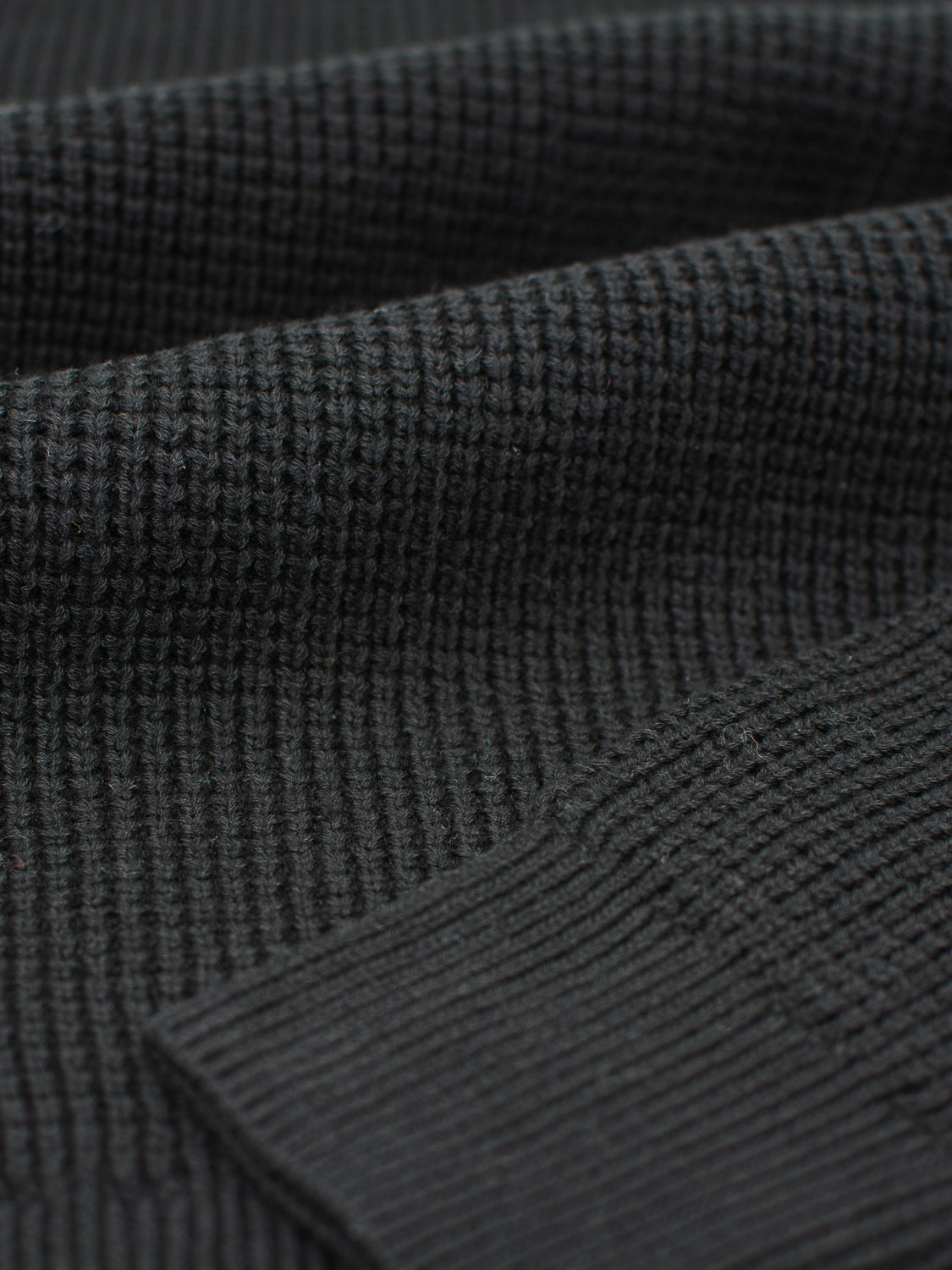 Close-up of a dark green Ragnar Waffle Knit Sweater from ID Menswear, made of 100% cotton. Its ribbed texture and fine stitching highlight its design, with the waffle knit softly folding to create shadows and depth.
