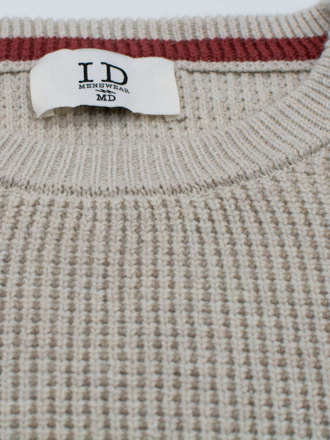 Close-up of the Ragnar Waffle Knit Sweater in beige by ID Menswear, featuring a ribbed collar with a red stripe. Made from 100% cotton, its waffle knit texture is visible. A white label reads ID Menswear, MD.