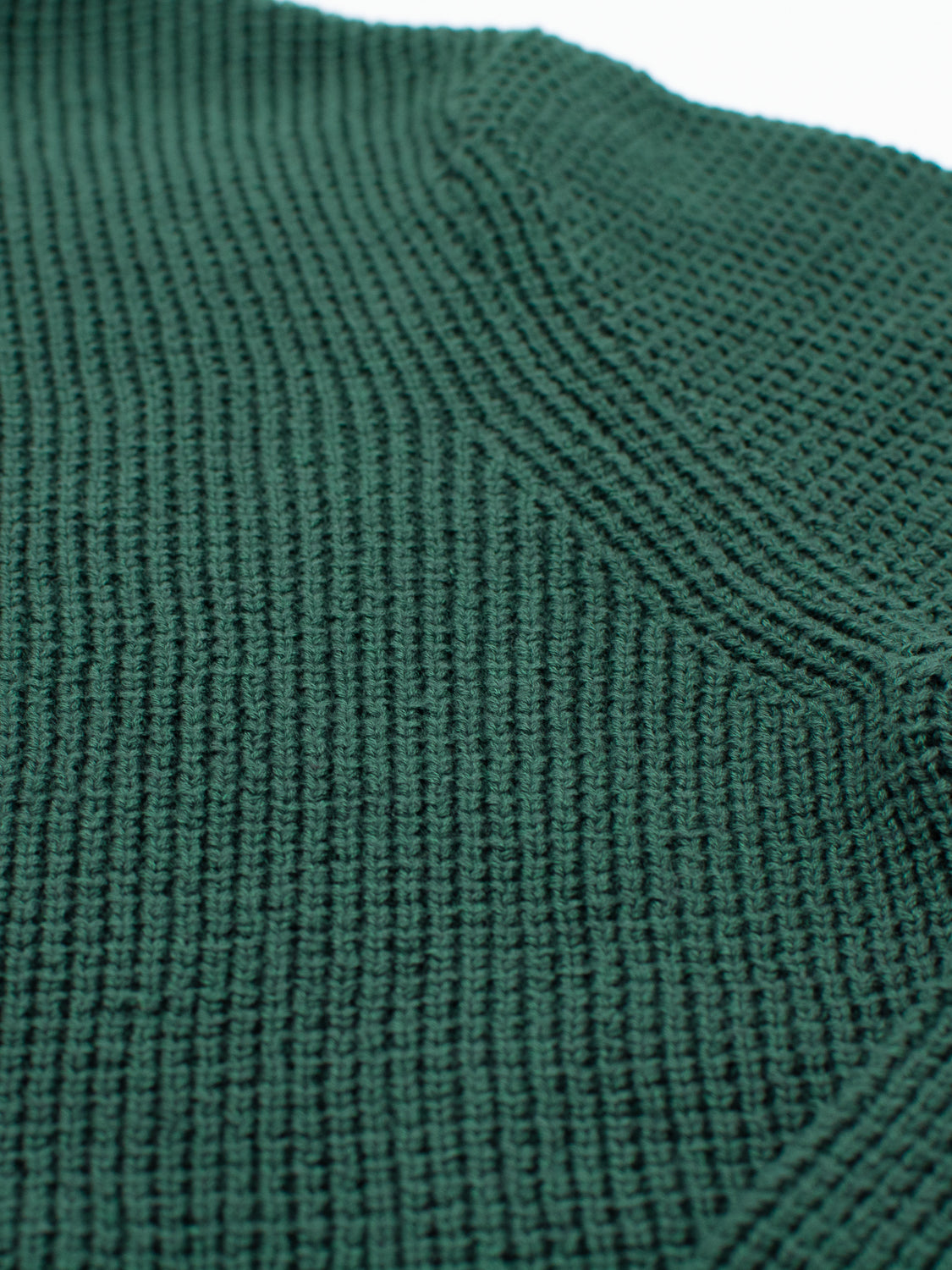 A close-up of a green textured waffle knit fabric from the Ragnar Waffle Knit Sweater by ID Menswear demonstrates its dense, tightly woven 100% cotton material. Lighting highlights the sweaters intricate pattern and depth.