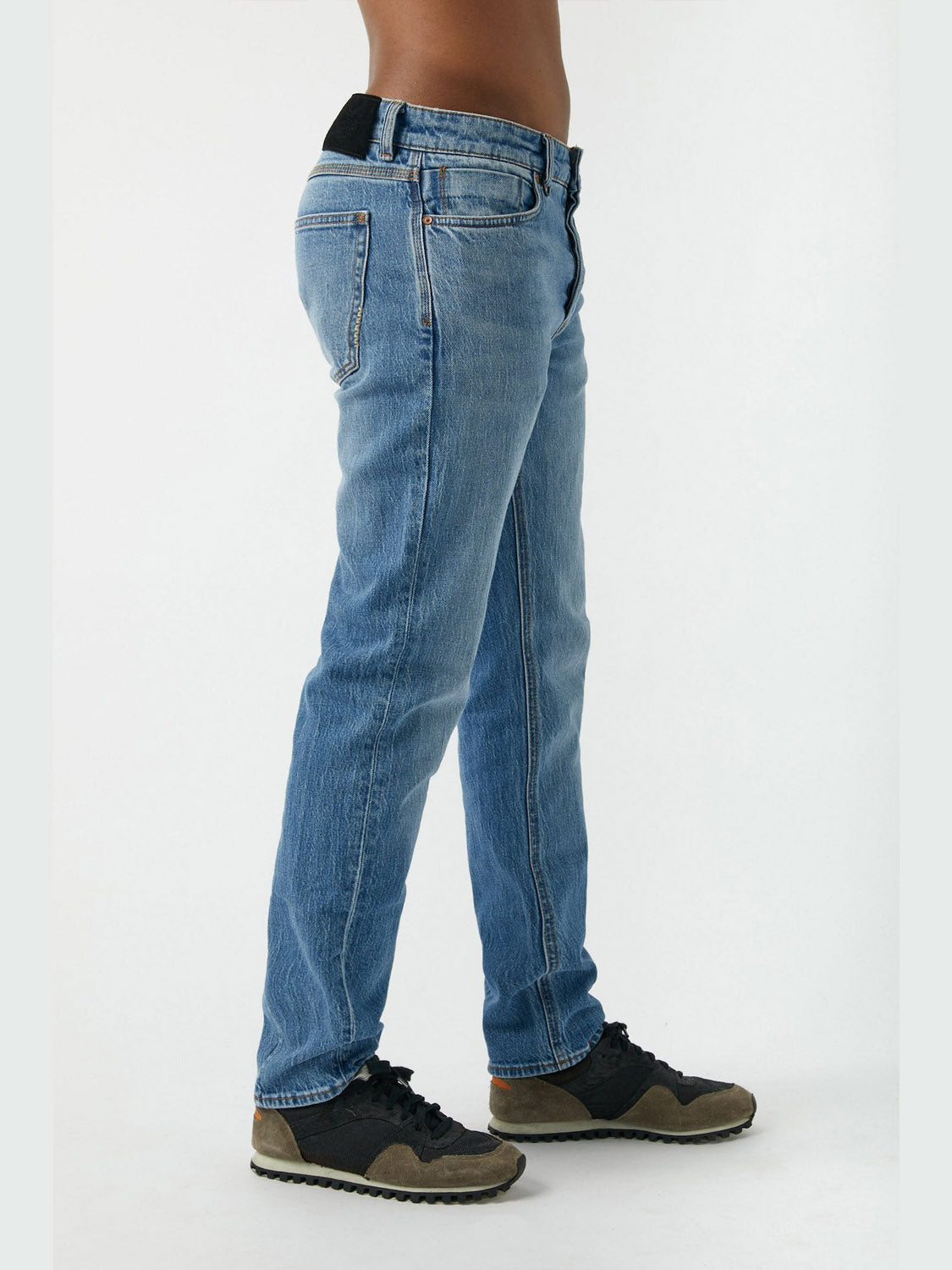 A person stands sideways against a plain light background, wearing Neuw Ray Straight Tempo jeans and black and brown sneakers, torso shown from waist down.