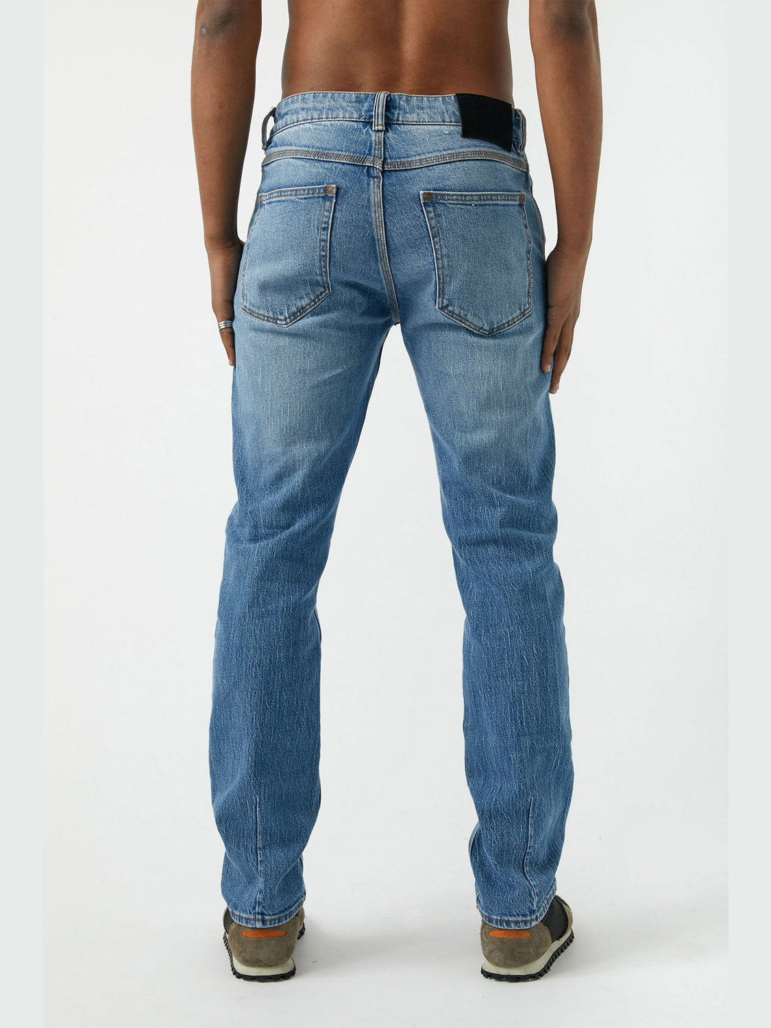 A person stands barefoot from the back, wearing Neuw Ray Straight Tempo vintage denim jeans with visible back pockets and a black patch on the waistband, set against a plain white background.