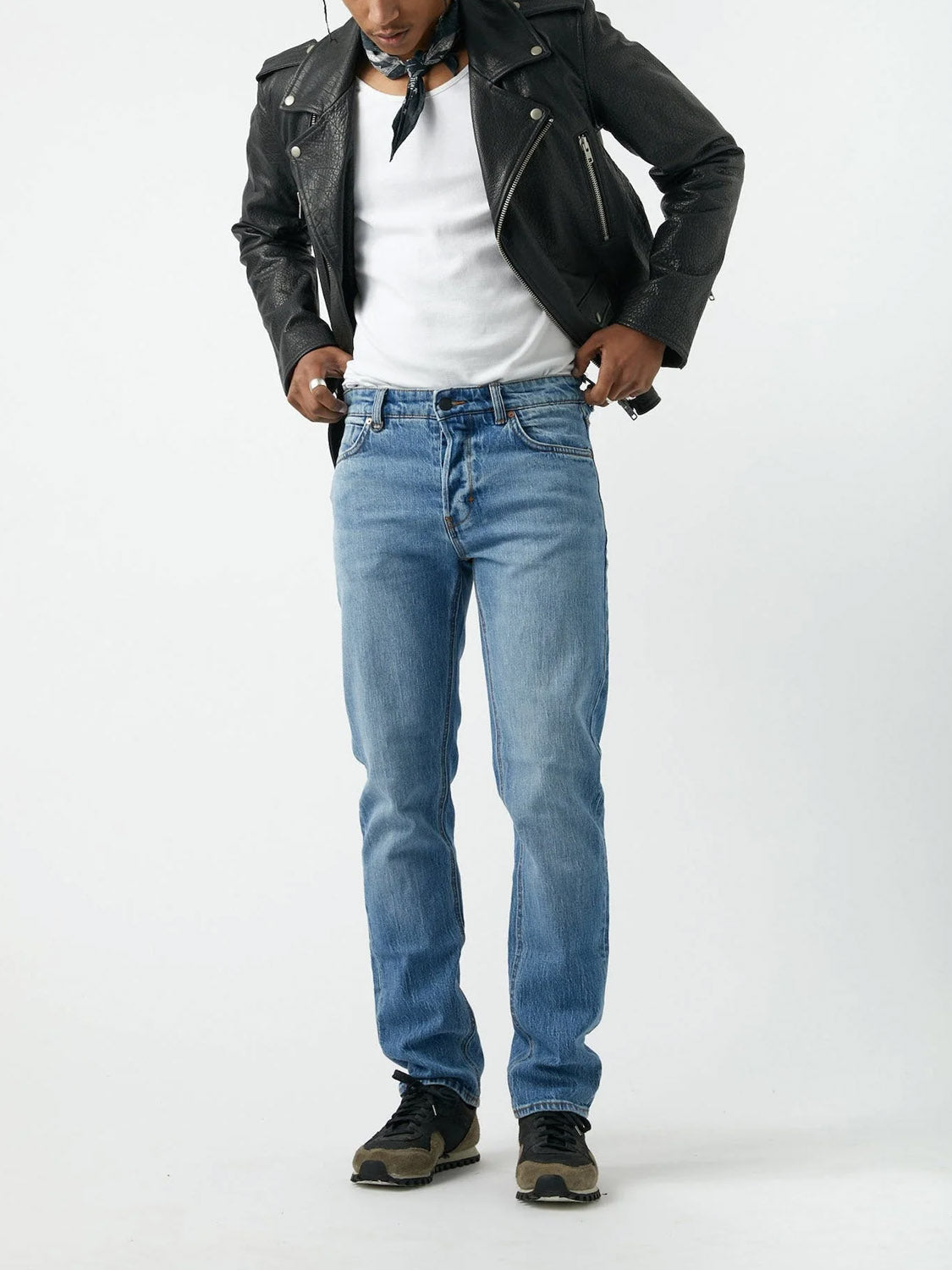 Wearing the Neuw Ray Straight Tempo vintage denim jeans with a black leather jacket, white shirt, black sneakers, and a neck bandana, the person stands against a plain white background, looking down and adjusting their jeans.