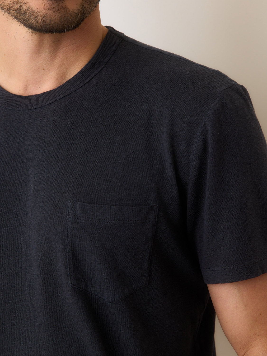 A person wearing the Marine Layer Relaxed Hemp Cotton Tee in dark blue featuring breathable fabric and a chest pocket. The image showcases their upper torso with part of their face visible against a neutral light background.