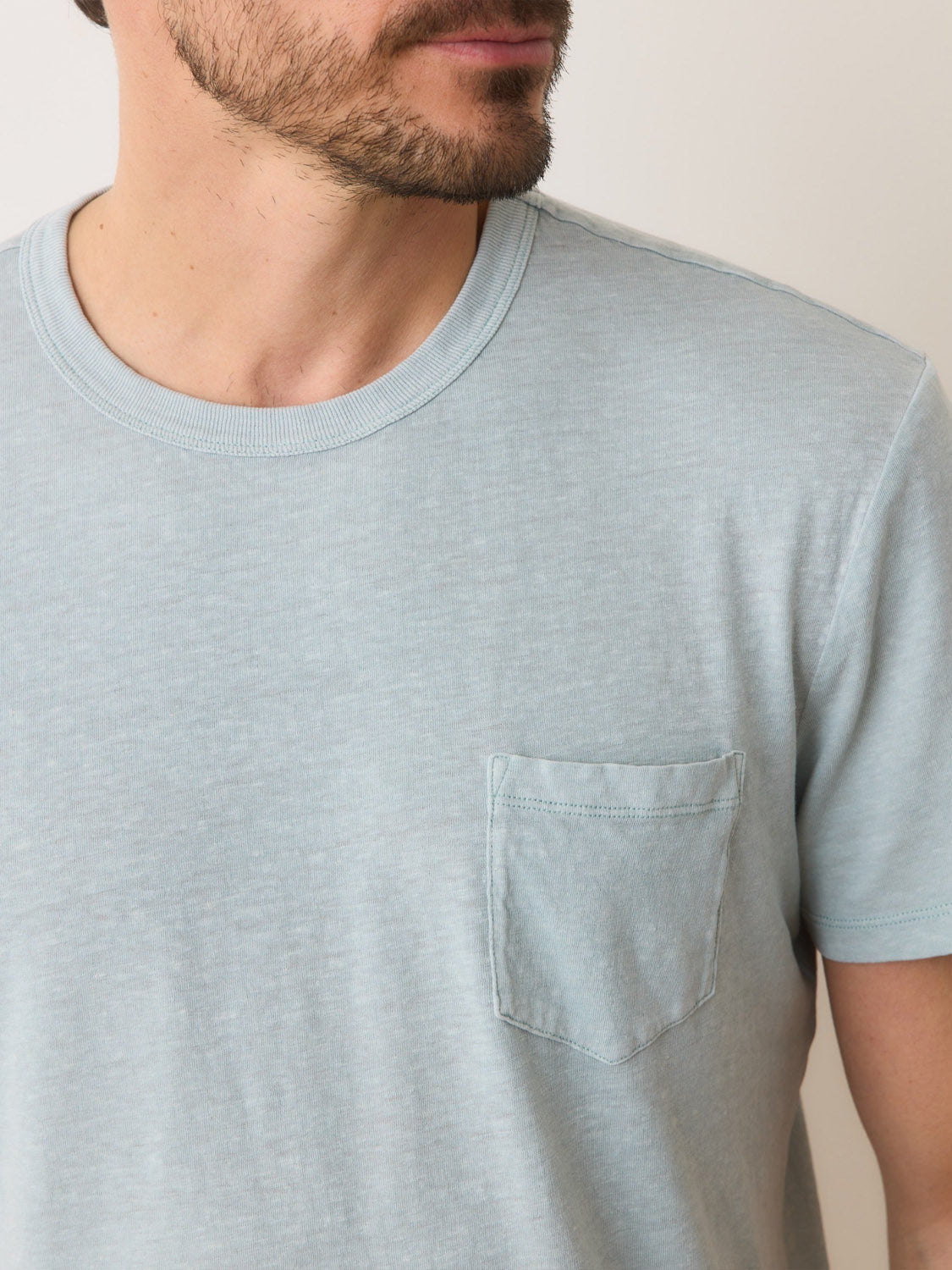 A person with a partial beard wears a Marine Layer Relaxed Hemp Cotton Tee, light gray and comfortable with a small chest pocket. The background is plain and light-colored, showing only the lower part of the face.