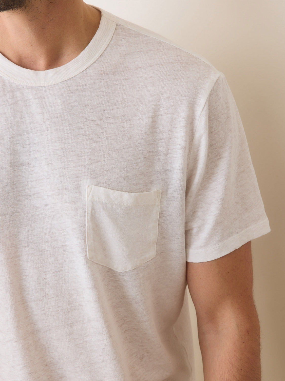 A person is partially visible wearing the Marine Layer Relaxed Hemp Cotton Tee by Marine Layer, a plain white, short-sleeve T-shirt with a small chest pocket, made from comfortable cotton and set against a neutral, light background.